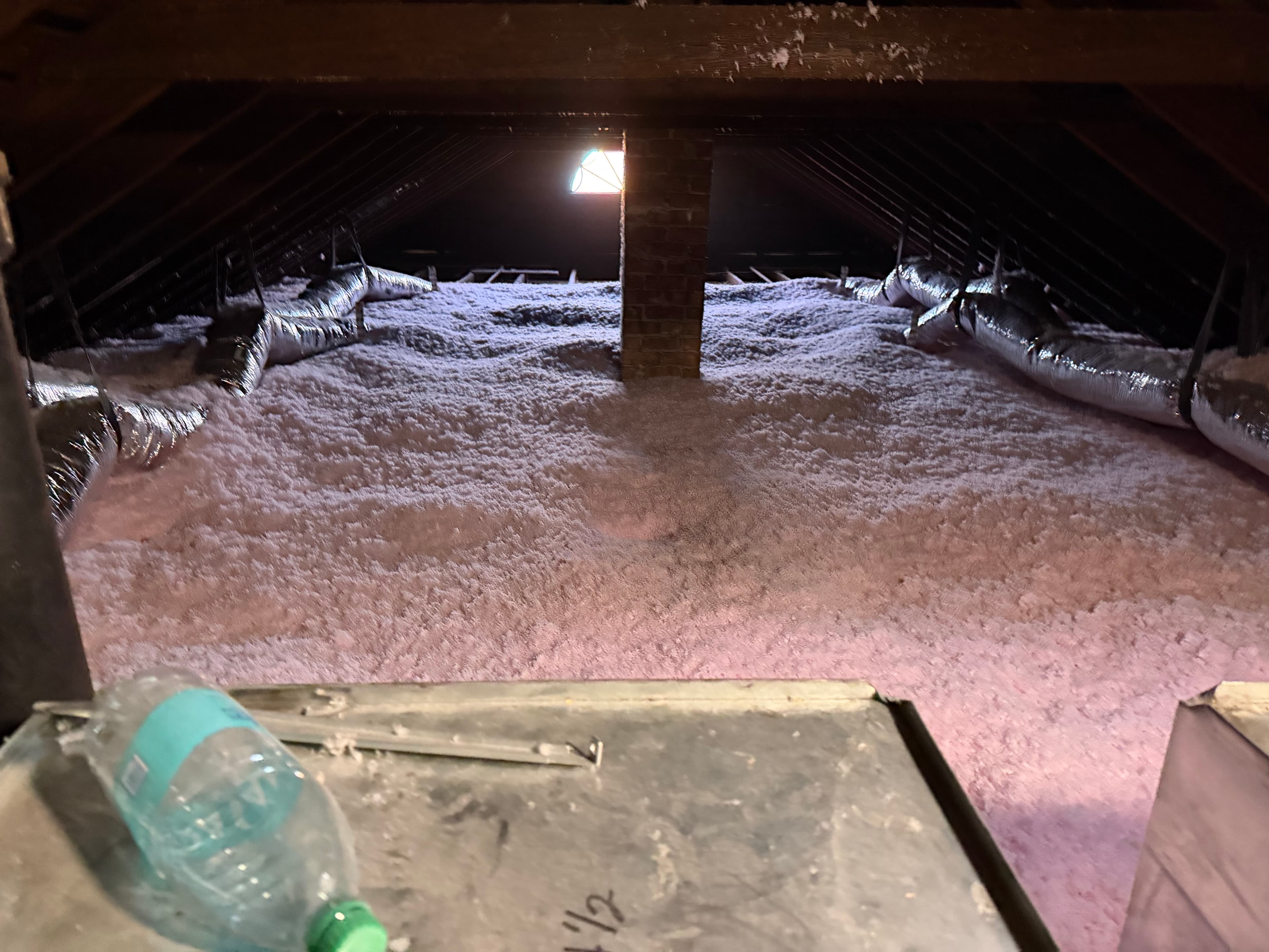 Attic space with thick pink insulation, silver HVAC ducts, and a central brick chimney stack.