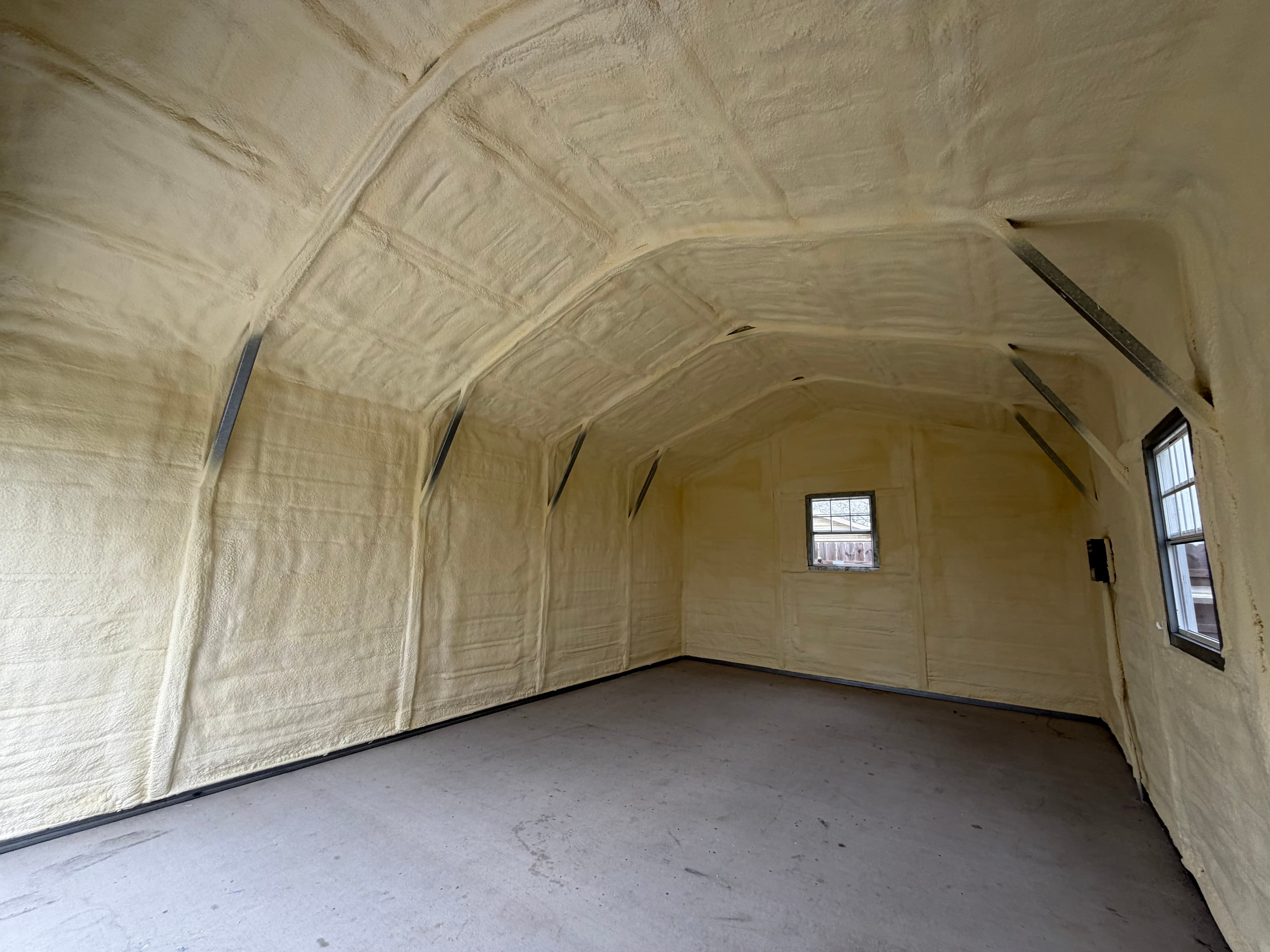 Empty shed interior with yellow spray foam insulation covering the walls and vaulted ceiling.