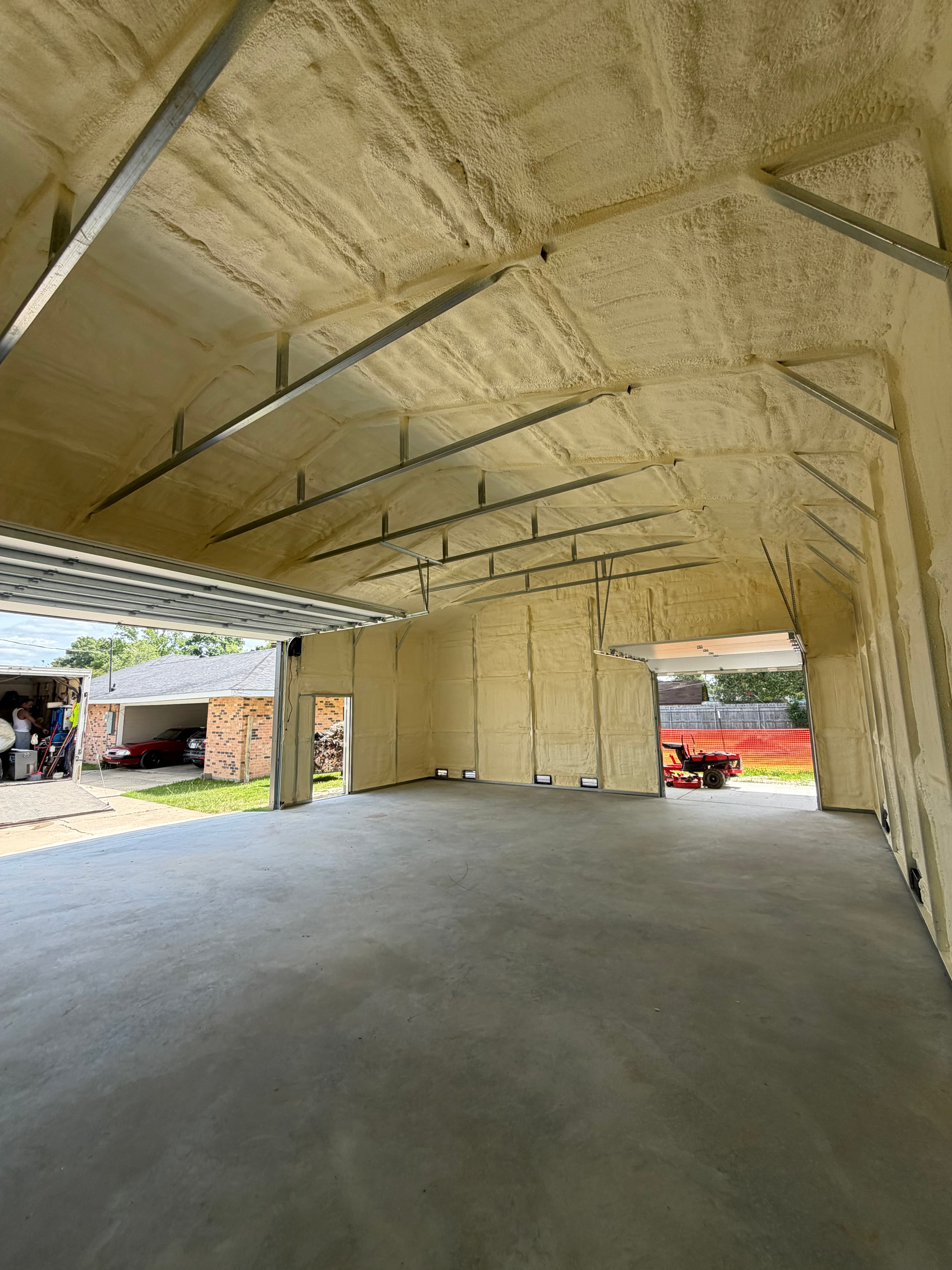 Spacious garage interior featuring yellow spray foam insulation on the walls and vaulted ceiling.