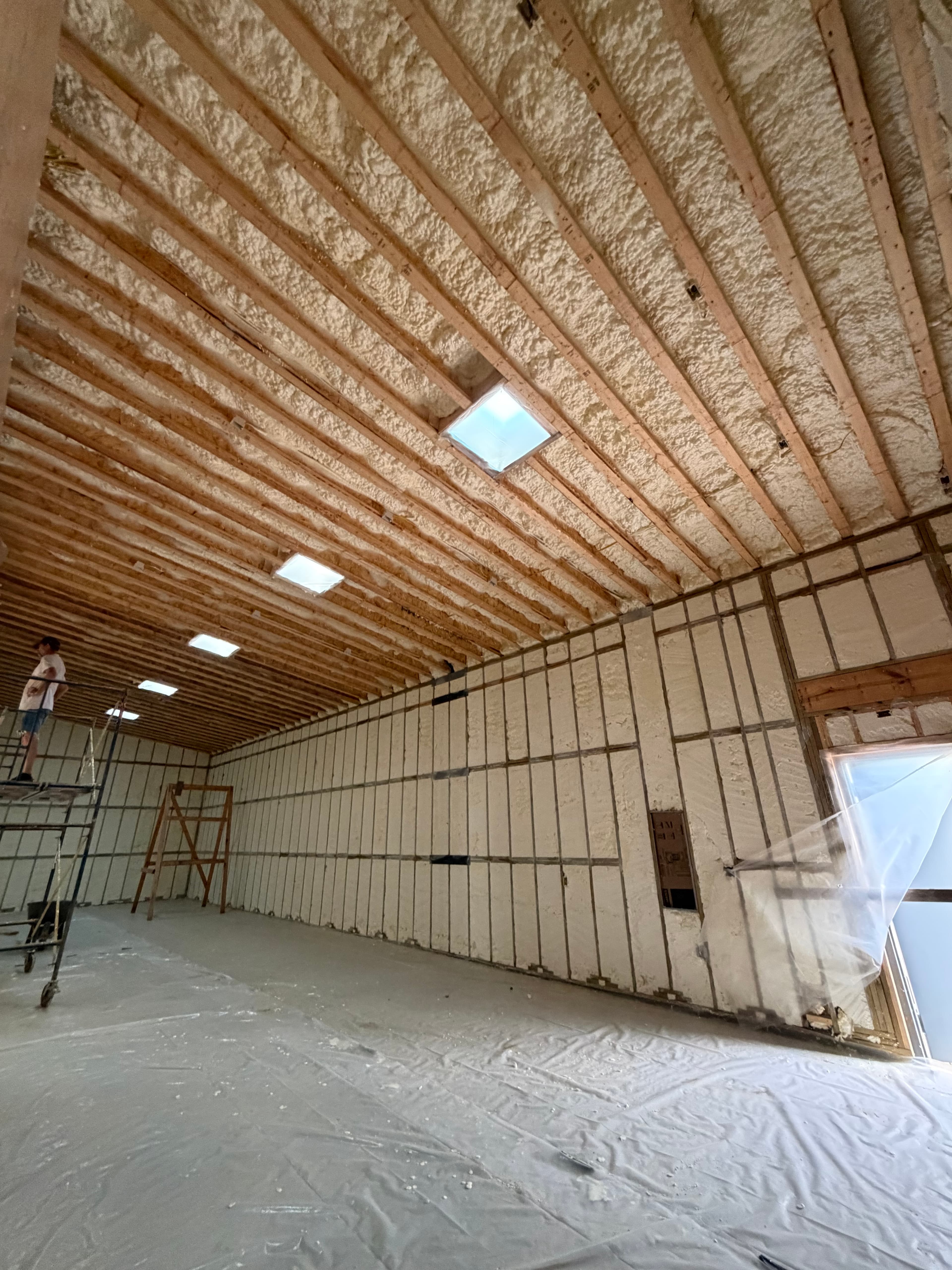 Spray foam insulation fills the walls and ceiling of a large room under construction with skylights.