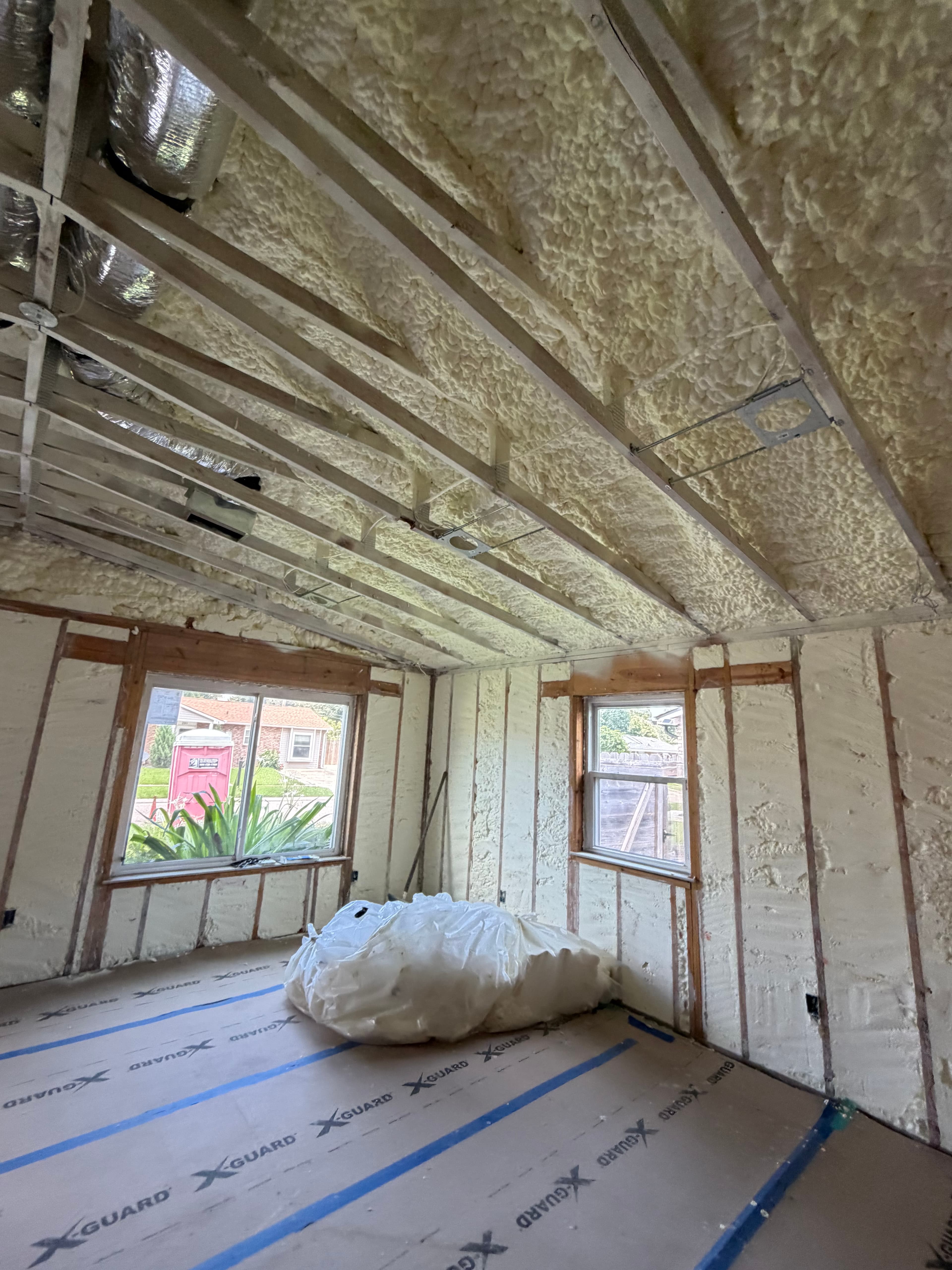 Room under construction with yellow spray foam insulation on walls and ceiling, featuring two windows.