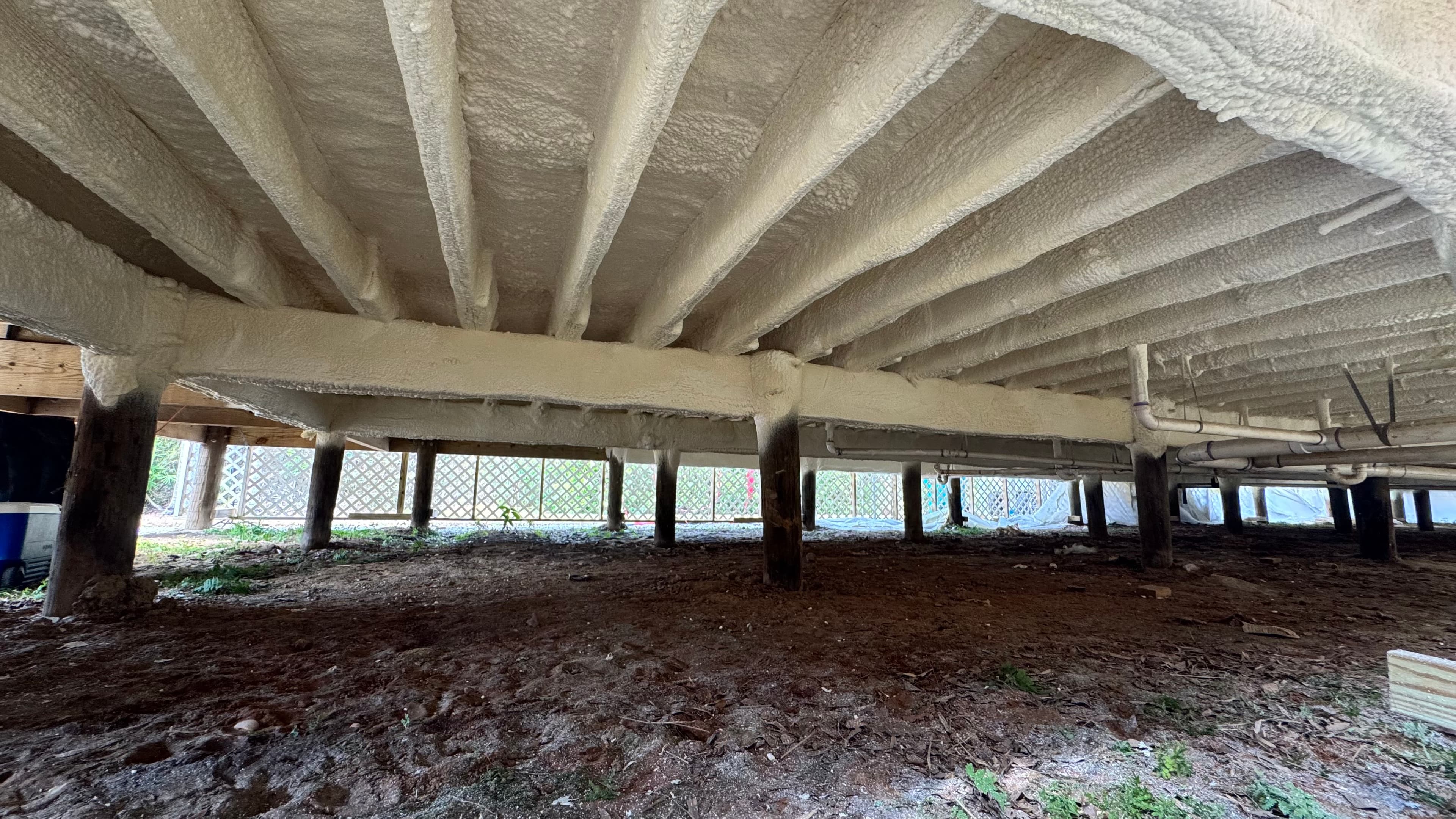 White spray foam insulation applied to the underside of floor joists in a crawl space.
