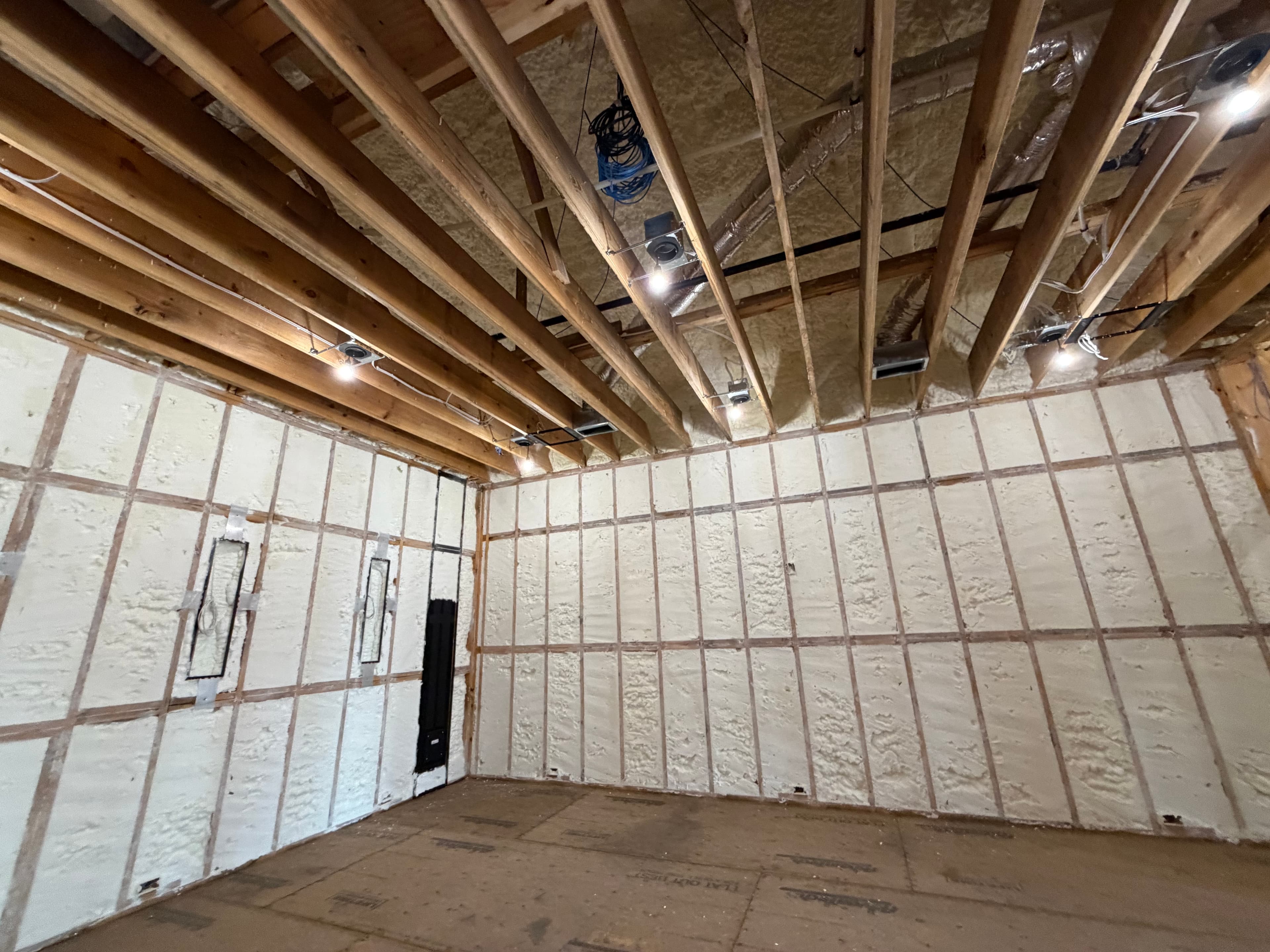 Spray foam insulation applied between wooden studs and ceiling rafters in an unfinished room.