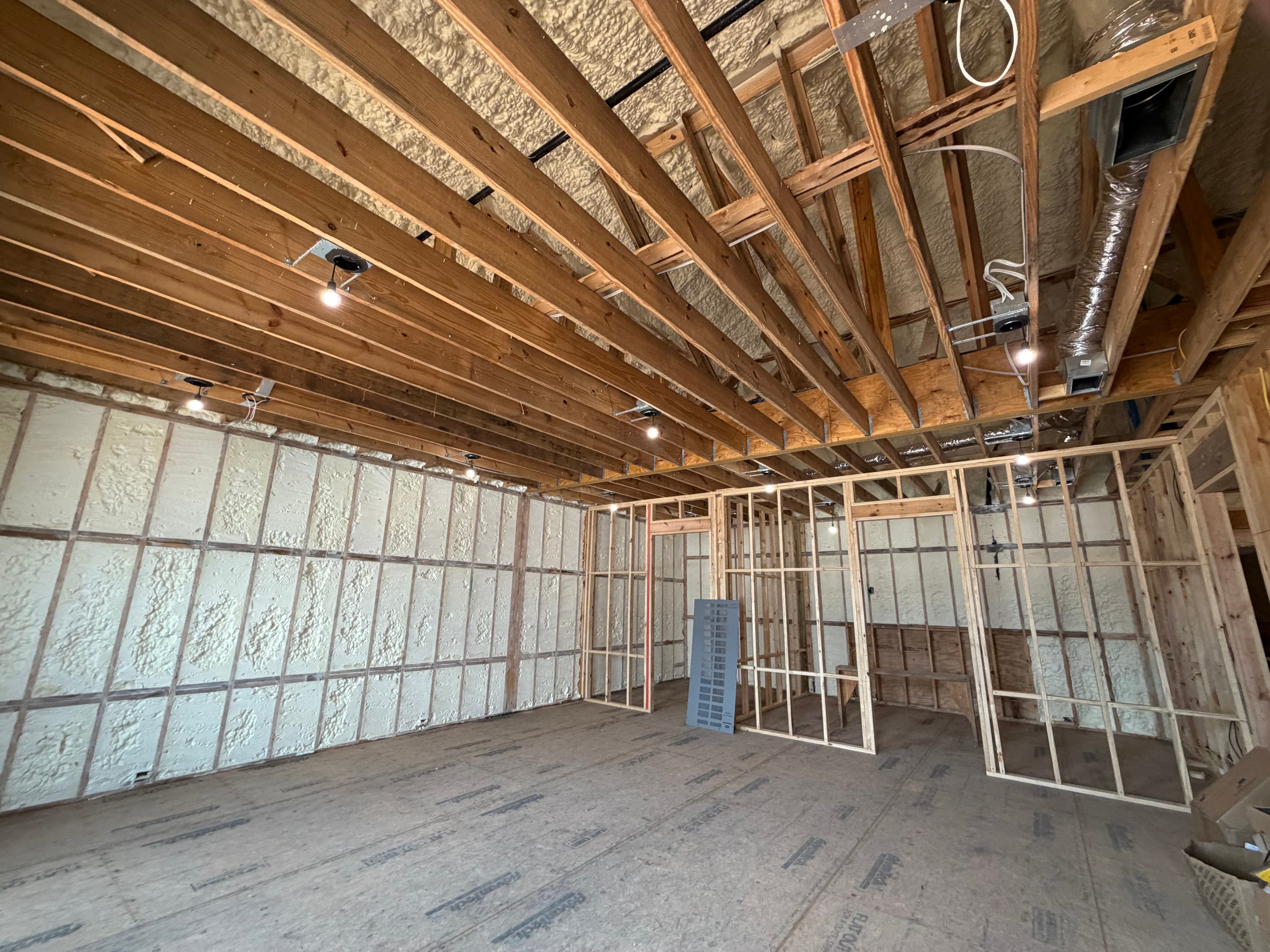 Interior construction site featuring wooden framing and spray foam insulation on walls and ceiling.