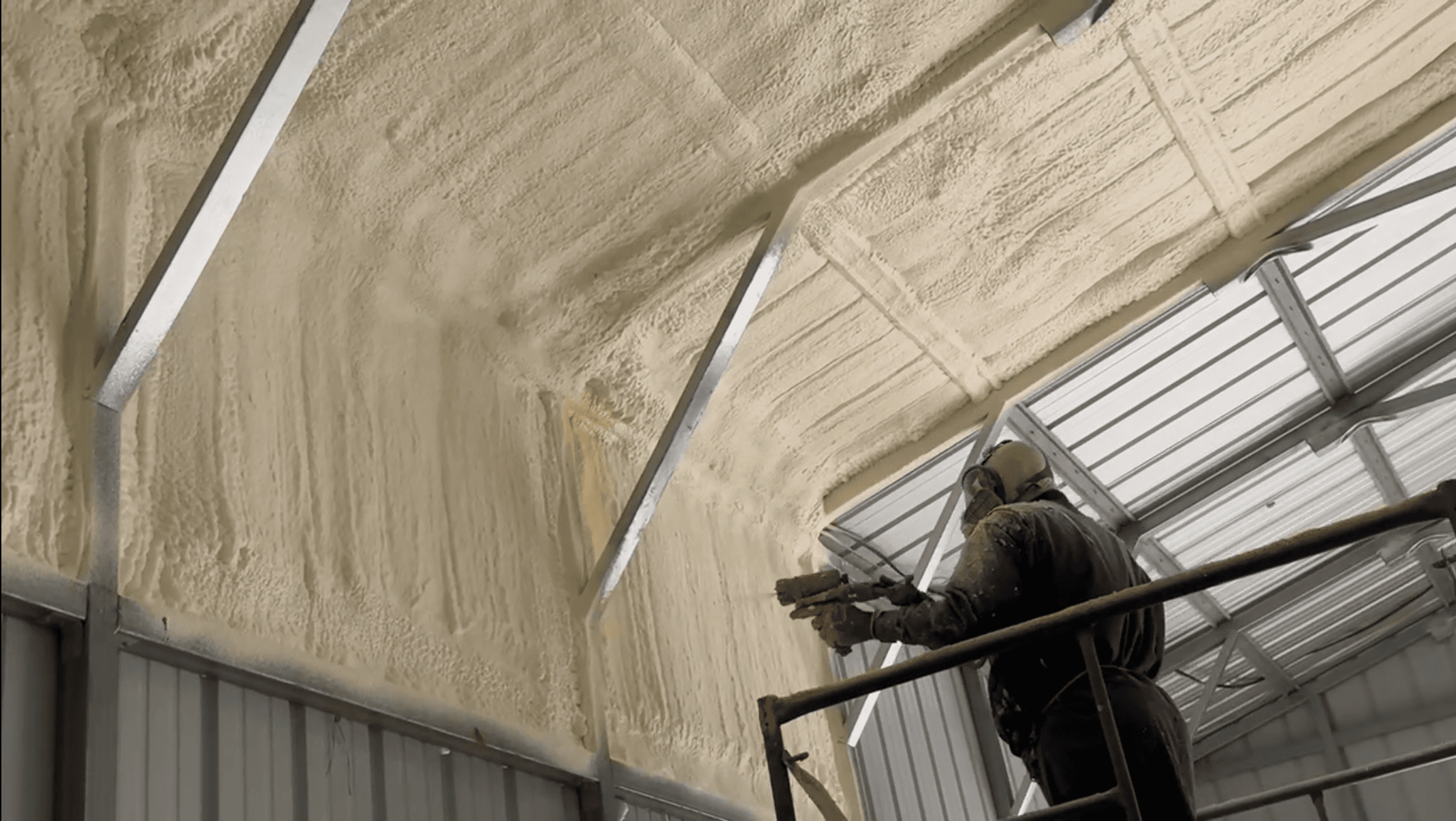Worker applying spray foam insulation to the interior walls and ceiling of a metal building.
