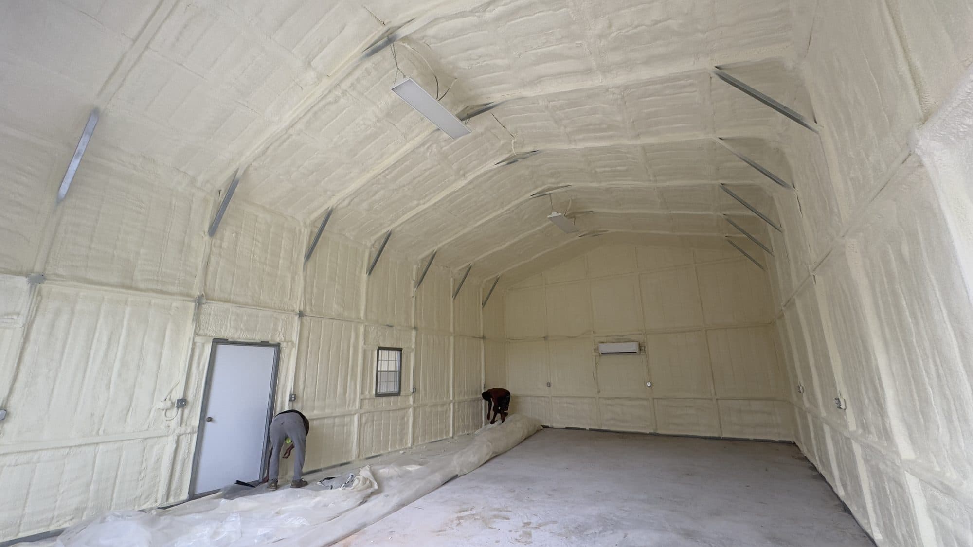 Interior of a large building with walls and ceiling covered in white spray foam insulation.