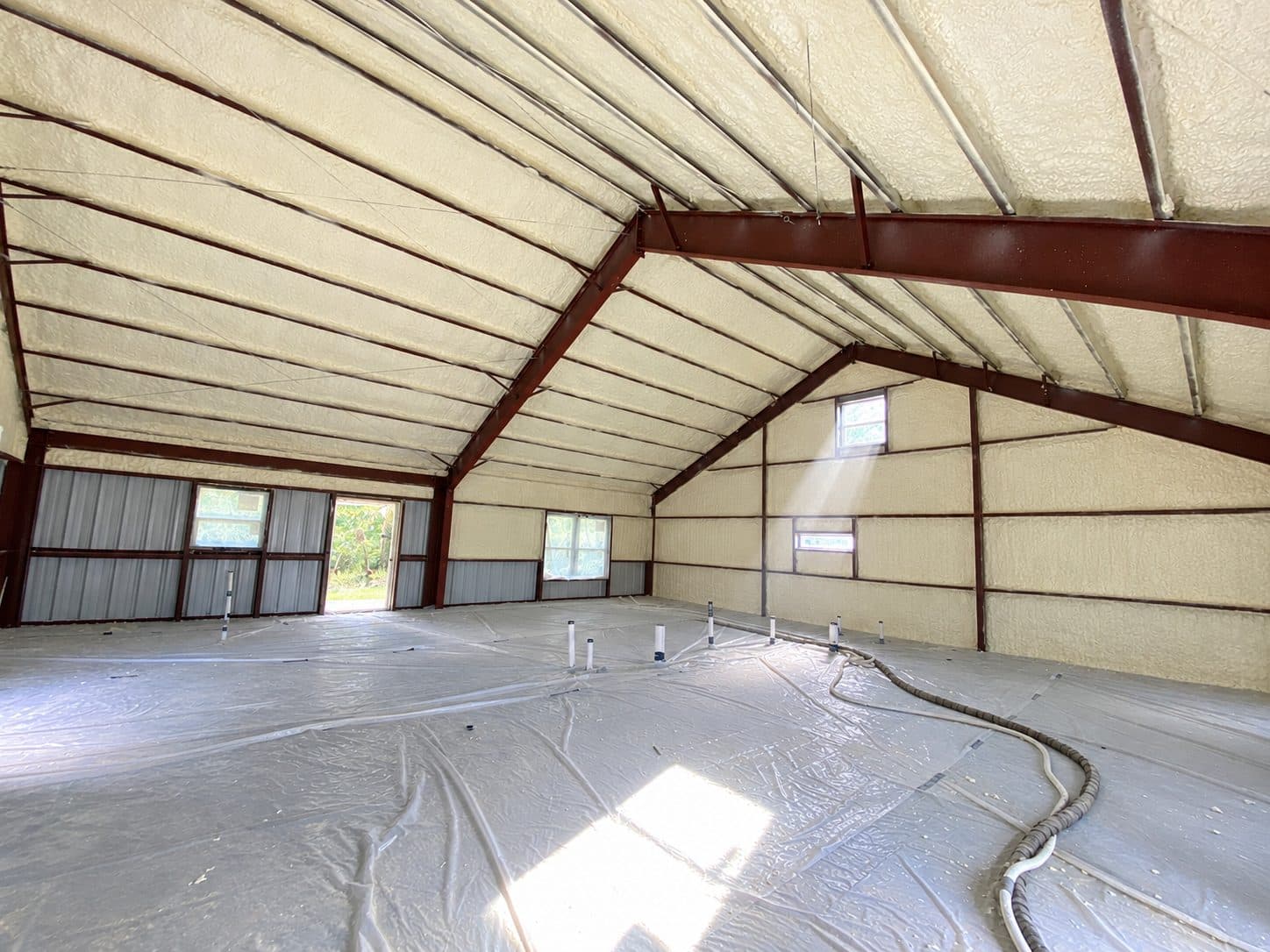 Interior of a large metal building with yellow spray foam insulation and plastic-covered floor.