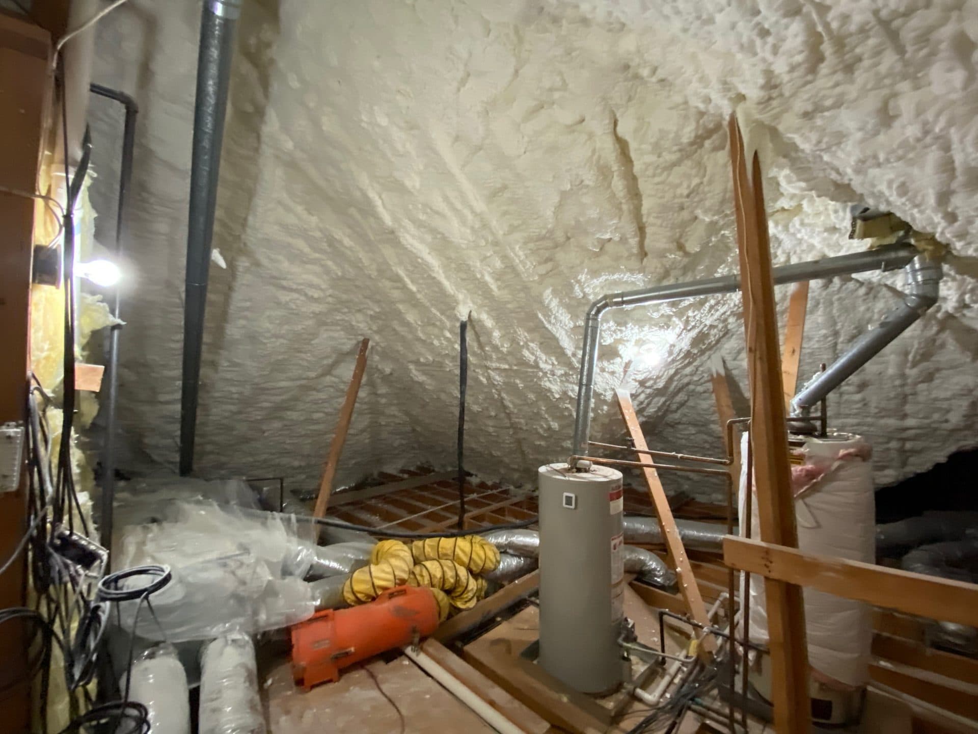 Spray foam insulated attic featuring a water heater, metal pipes, and an orange portable heater.