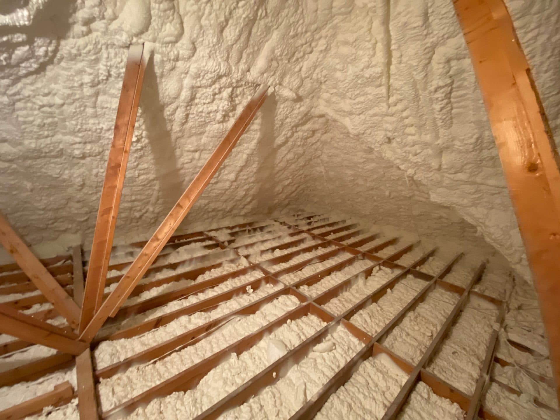 White spray foam insulation applied to the roof and floor joists of a wooden attic.