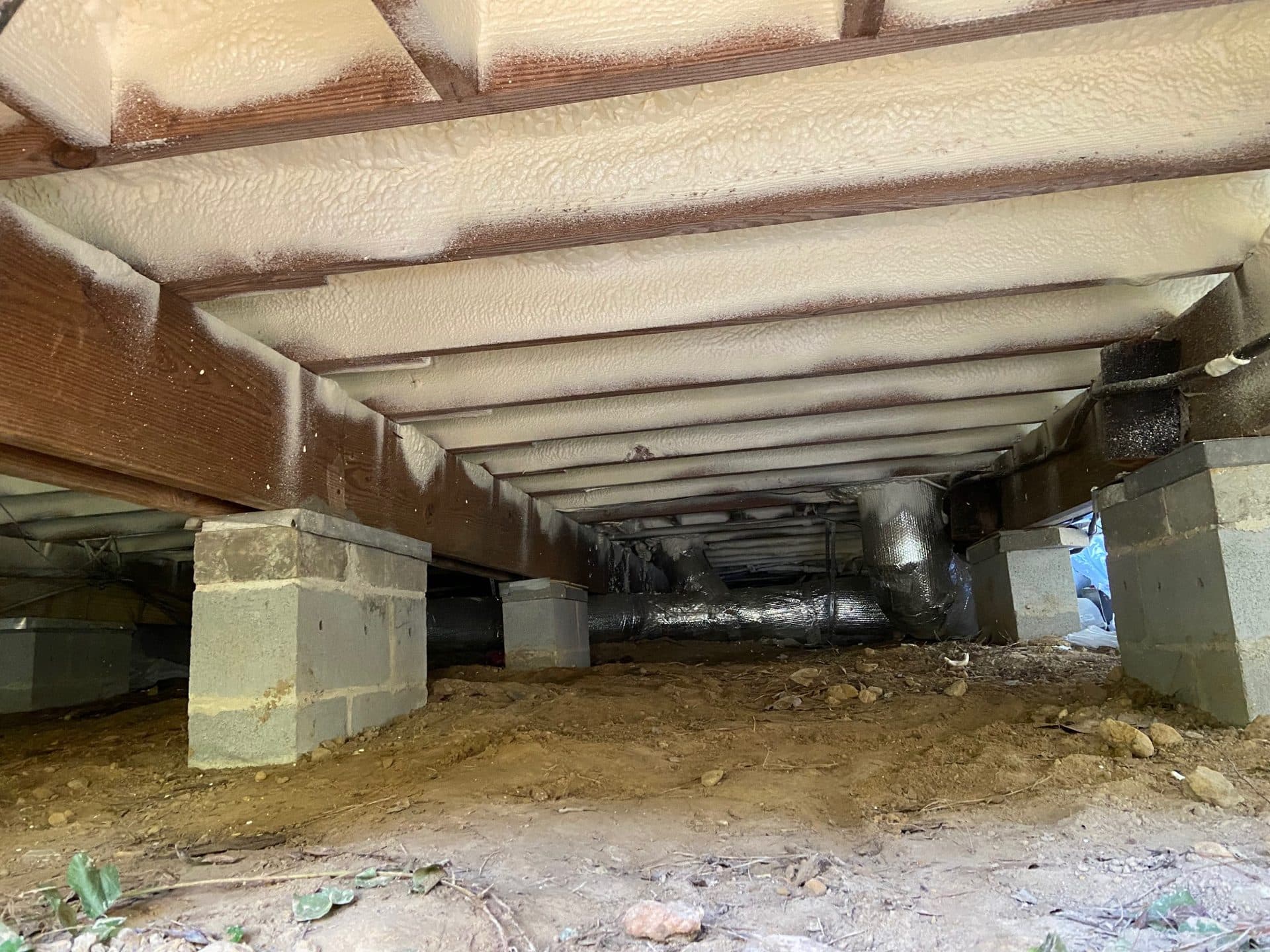 Crawl space with spray foam insulation on joists, concrete block piers, and insulated ductwork.