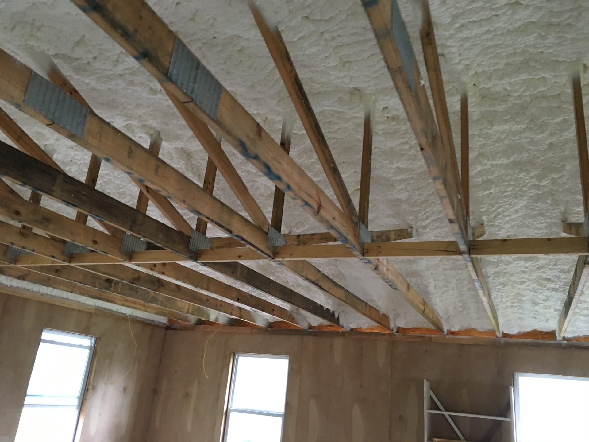 White spray foam insulation applied between wooden roof trusses in a building under construction.