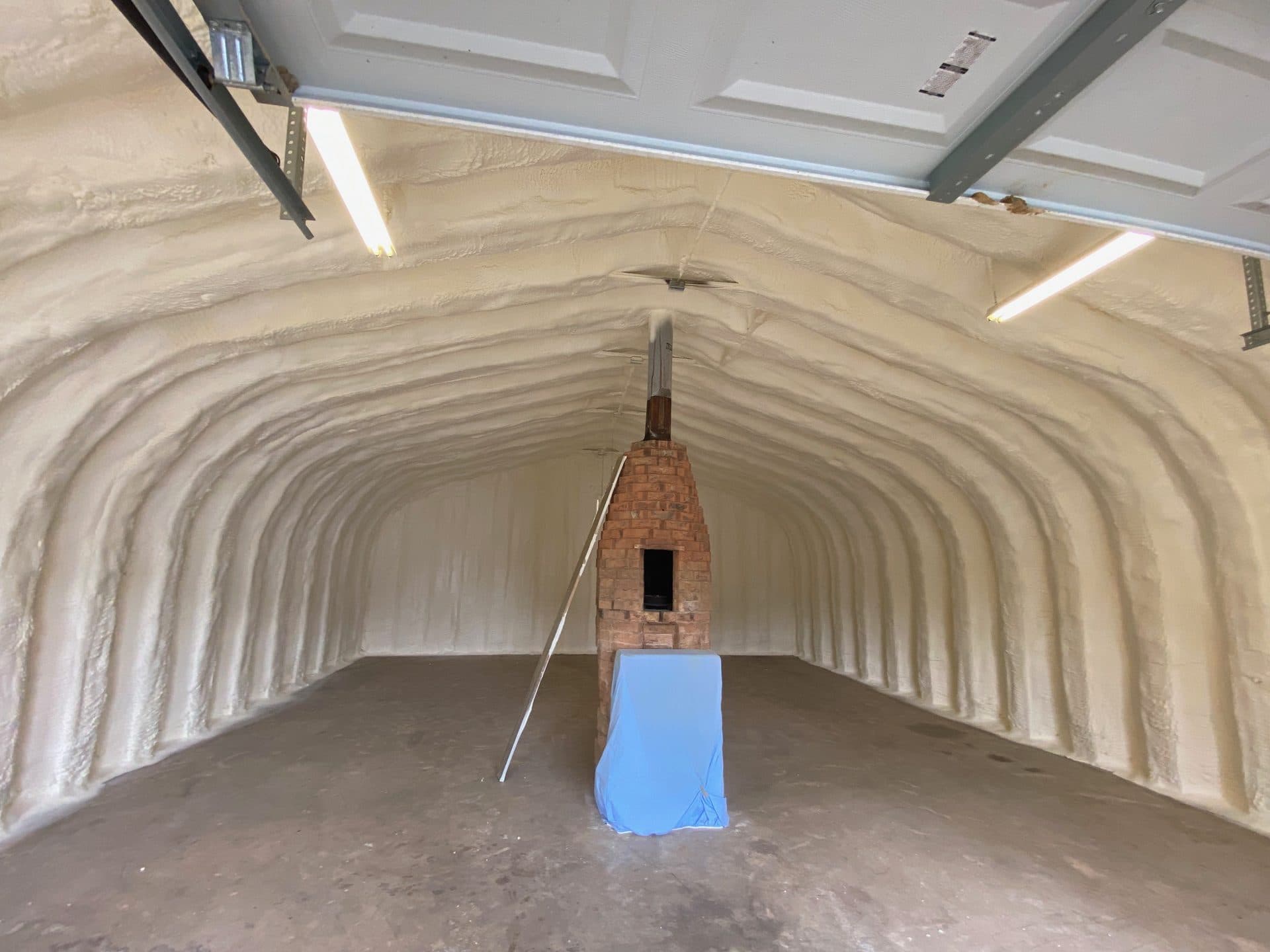 Large arched interior with white spray foam insulation featuring a central brick kiln and chimney.