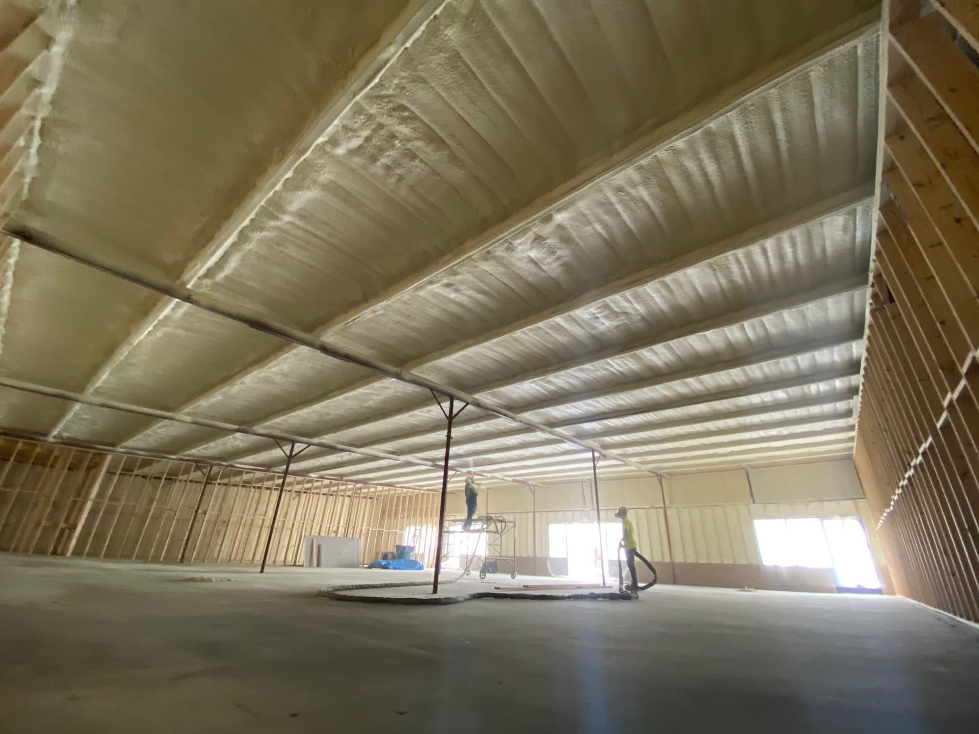Spray foam insulation on the ceiling of a large building under construction with wooden framing.