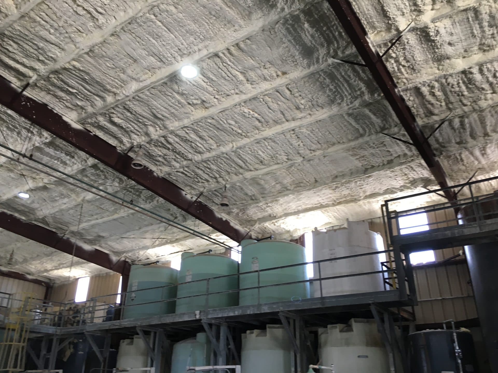 Industrial storage tanks on a platform beneath a ceiling with thick spray foam insulation.