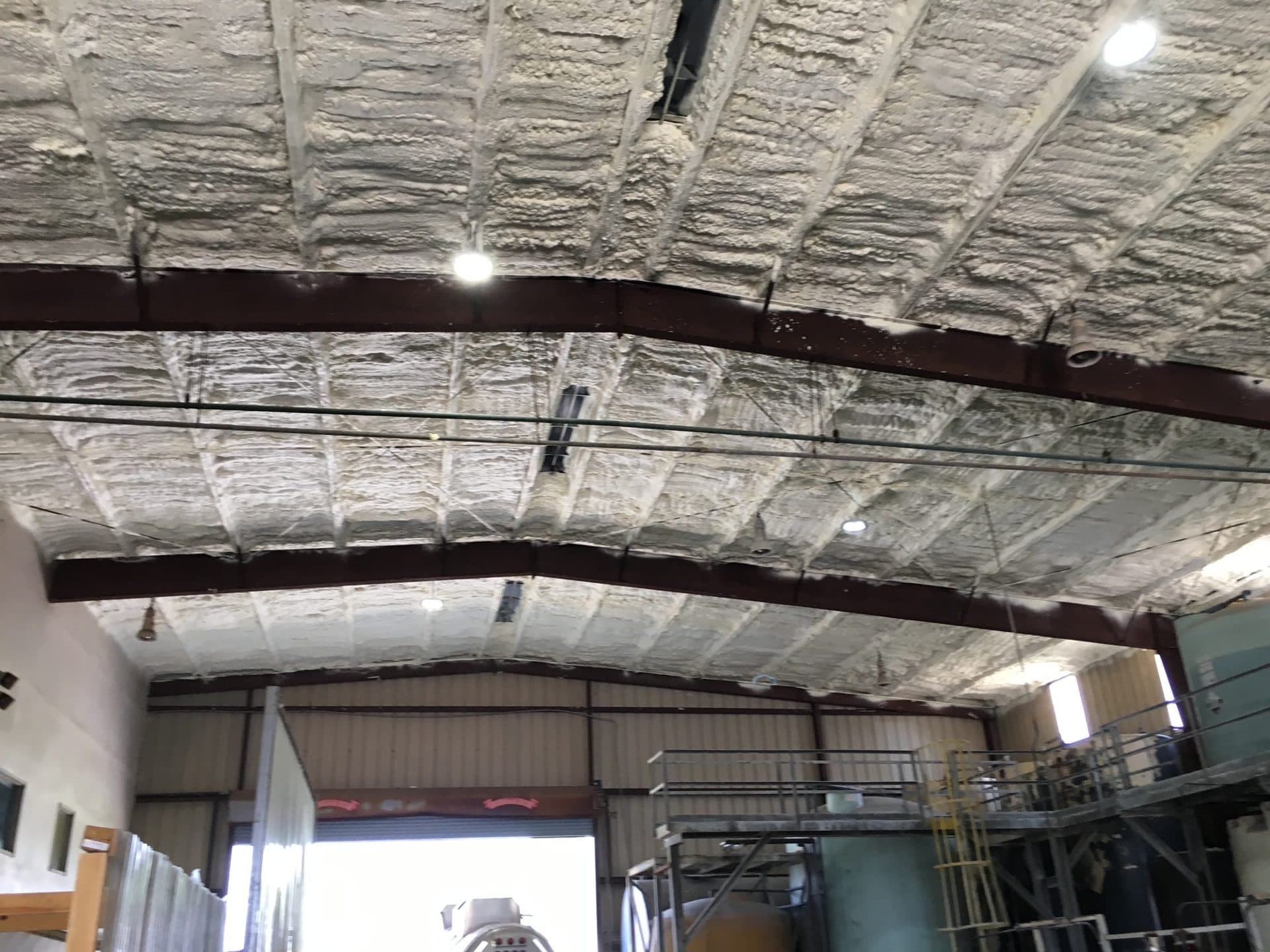 Industrial warehouse interior with white spray foam insulation on the ceiling and dark steel beams.