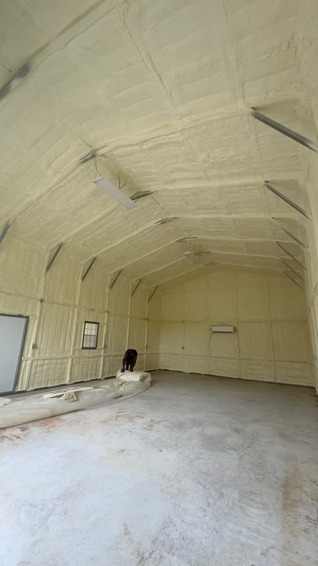 Large empty building interior with spray foam insulation covering the walls and high arched ceiling.