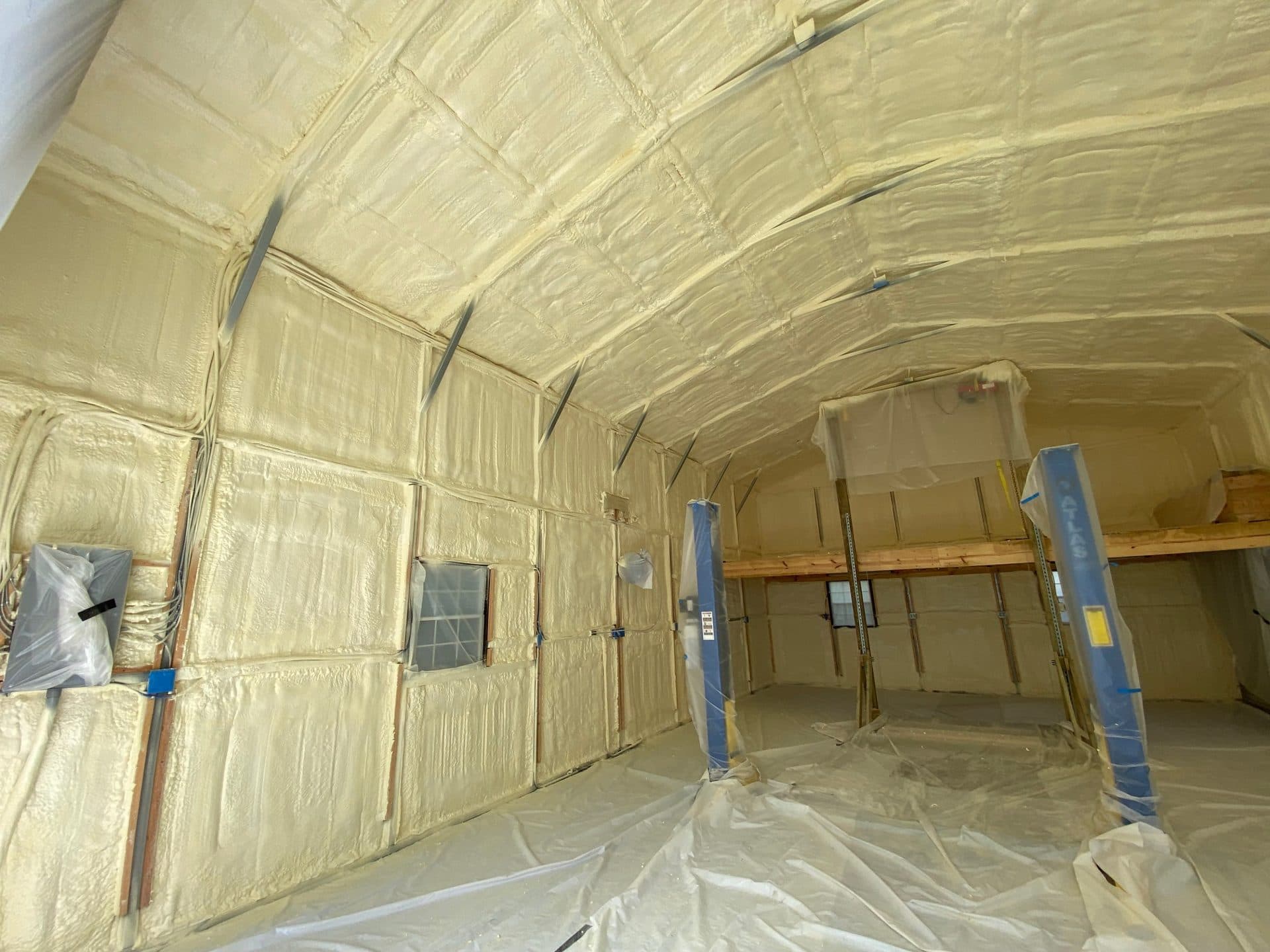 Yellow spray foam insulation covers the interior walls and arched ceiling of a large workshop.