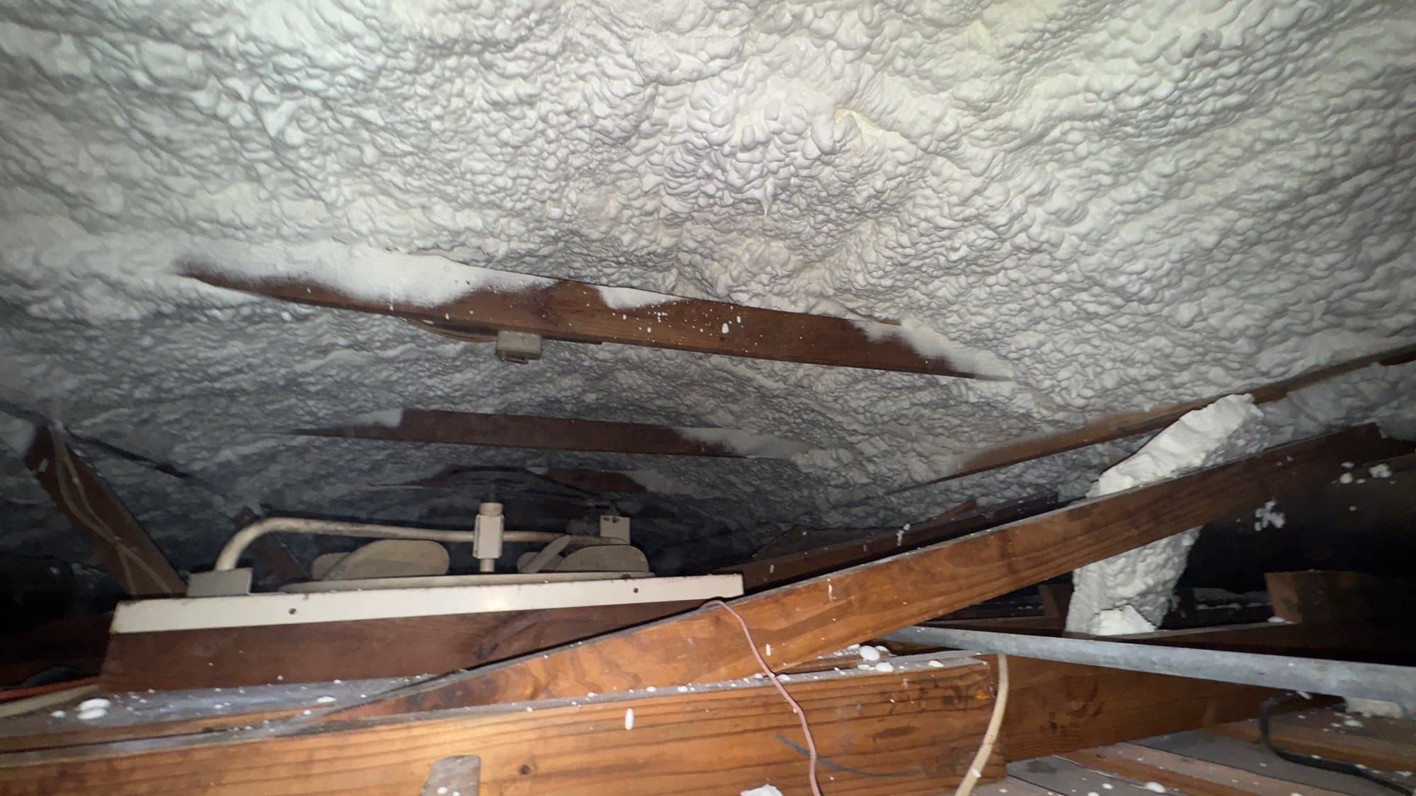 White spray foam insulation applied to the underside of a roof between wooden attic rafters.