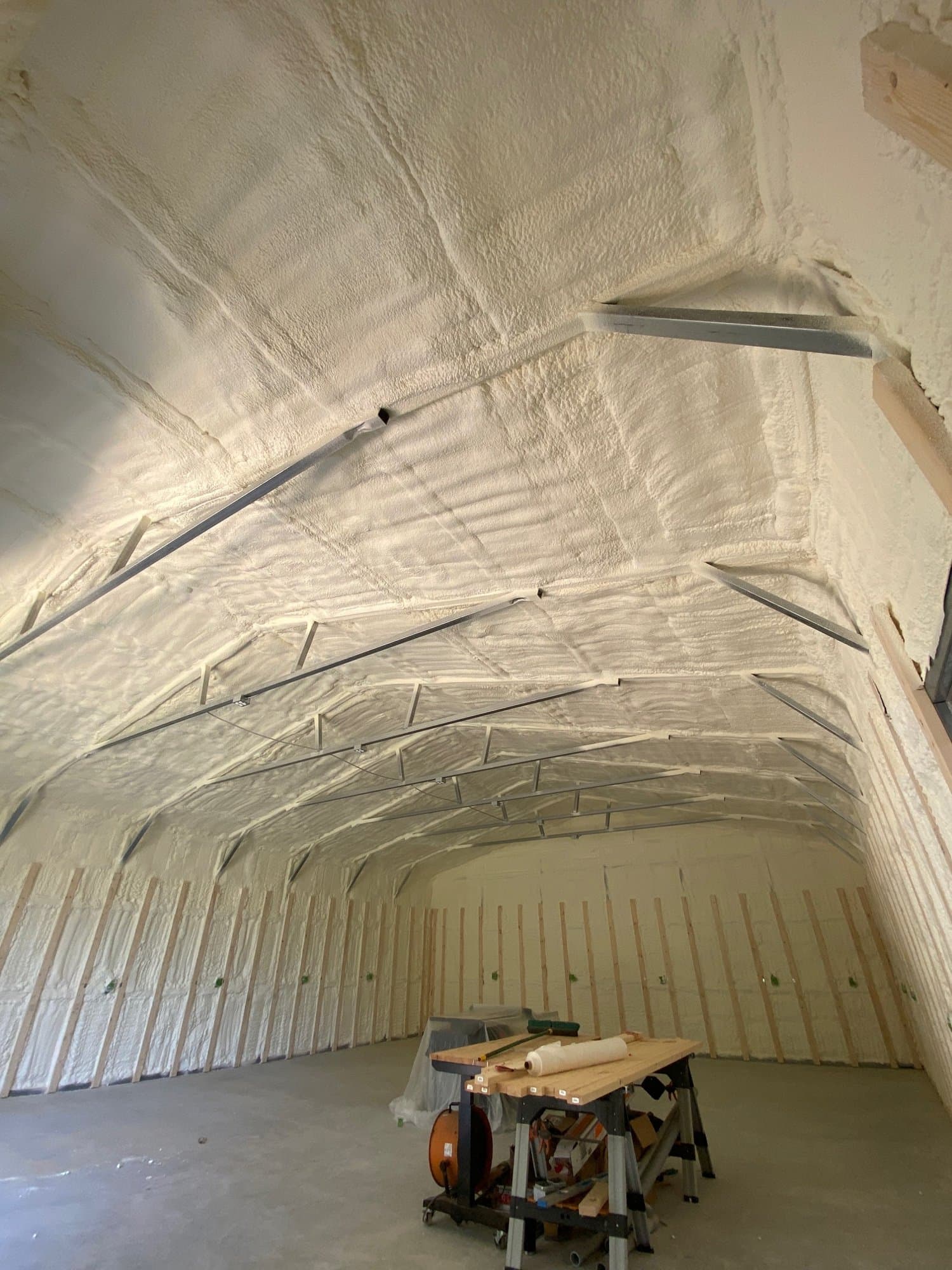 Interior of a building with white spray foam insulation covering the walls and curved ceiling.