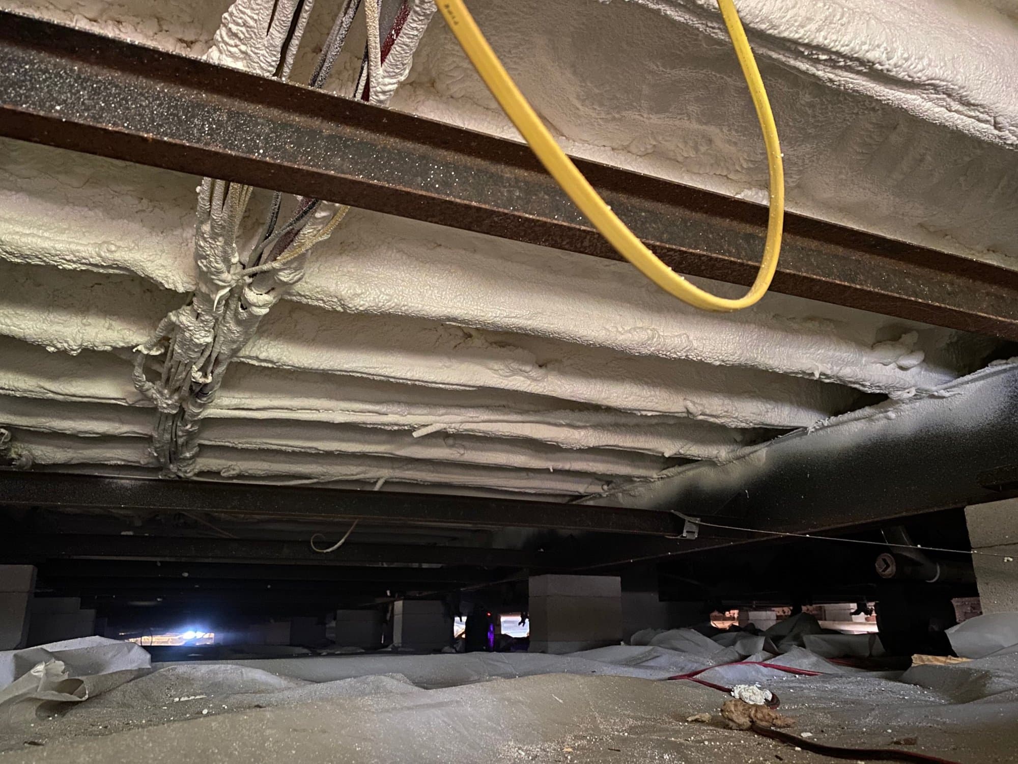 White spray foam insulation covers the underside of a floor supported by steel beams.