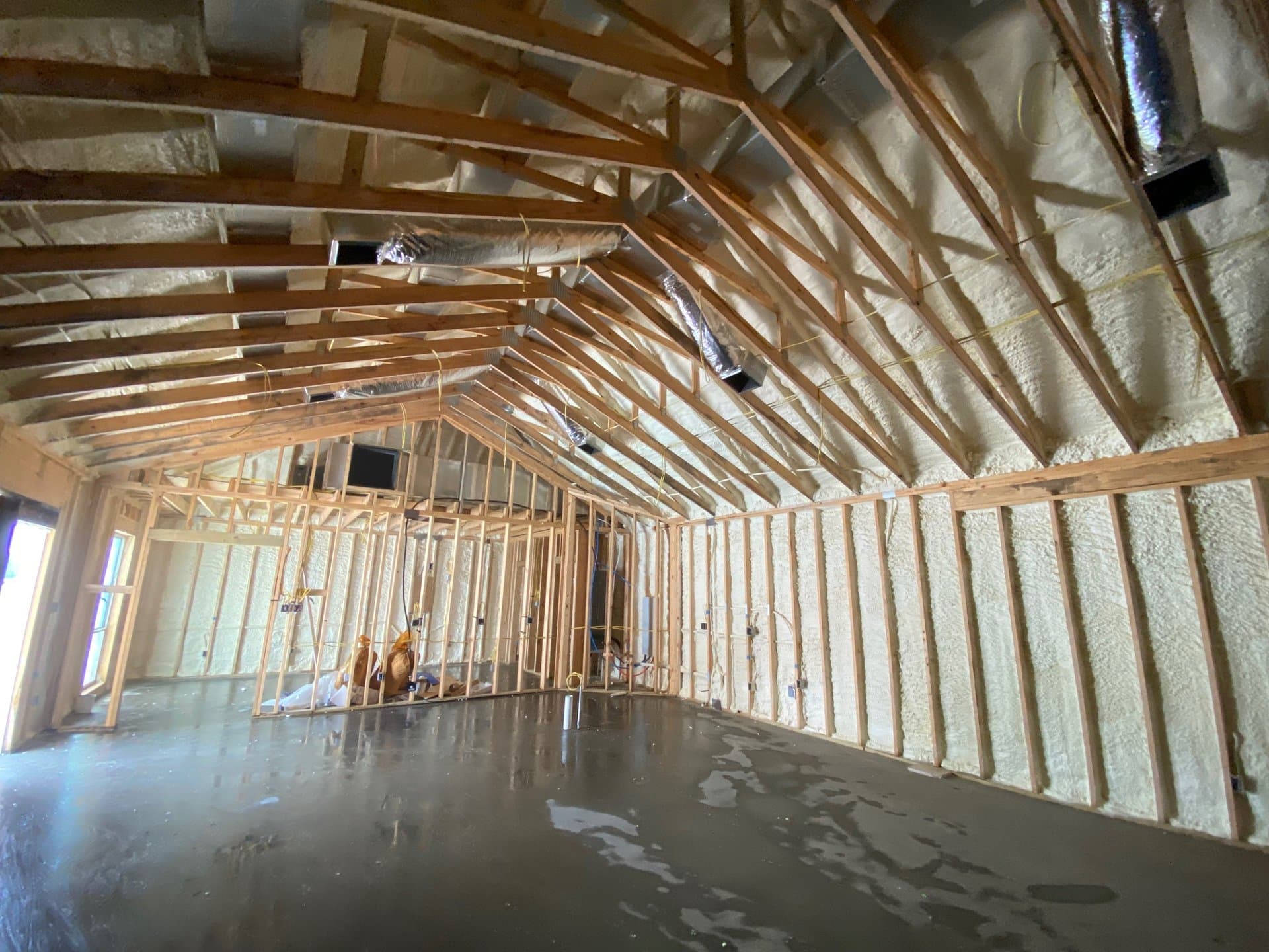 Building interior under construction with wooden framing, spray foam insulation, and a concrete floor.