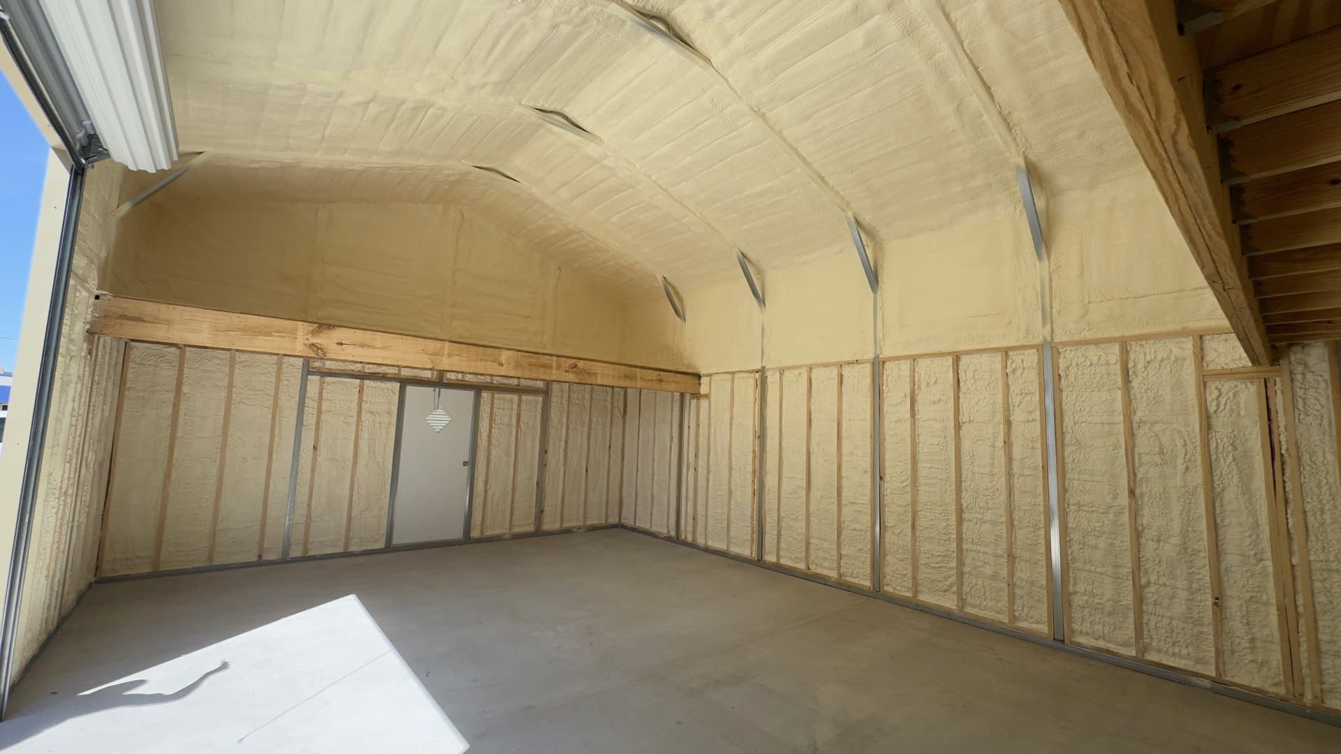 Interior of a structure with yellow spray foam insulation covering the walls and vaulted ceiling.