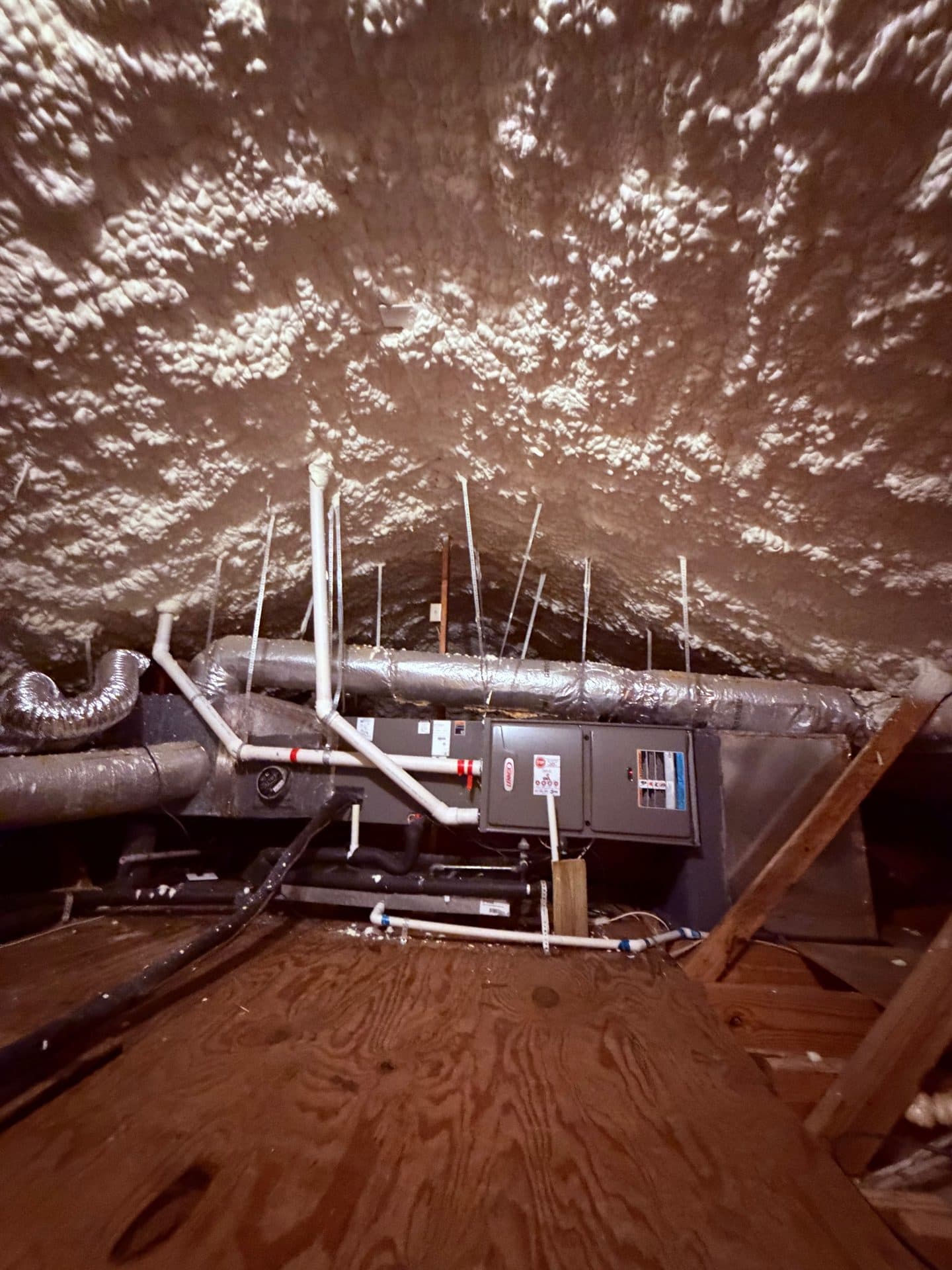 HVAC system and ductwork in an attic with white spray foam insulation on the ceiling.