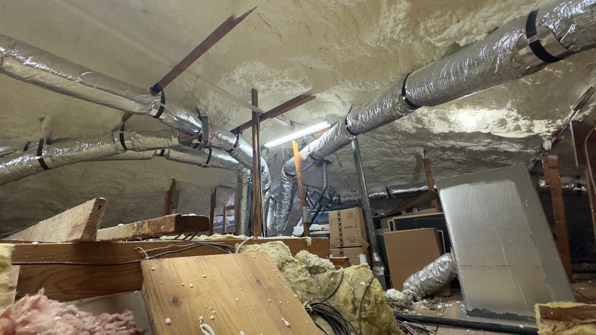 Attic interior featuring spray foam insulation on the ceiling and flexible silver HVAC ductwork.