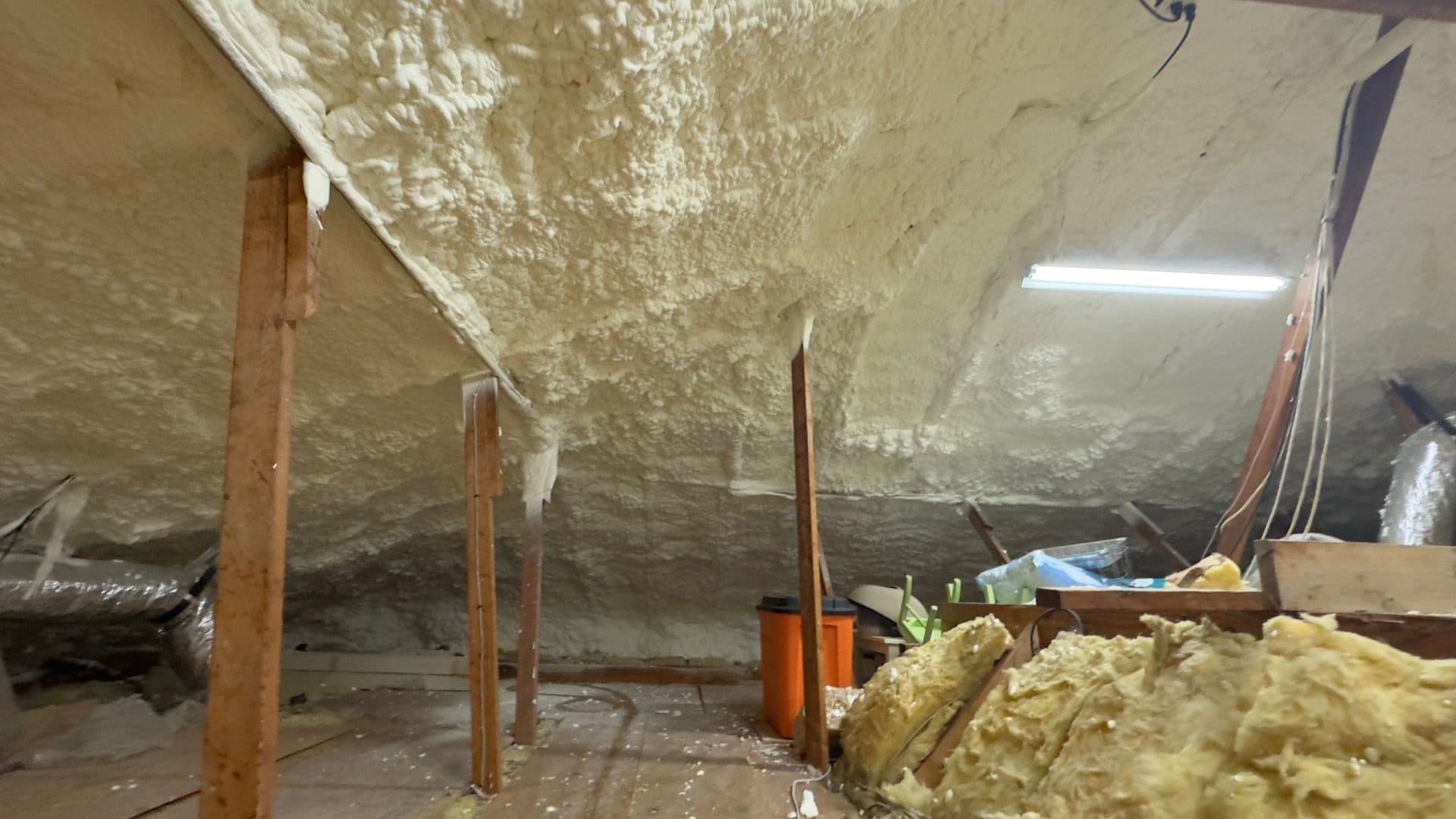 Thick white spray foam insulation applied to the ceiling and walls of a residential attic.