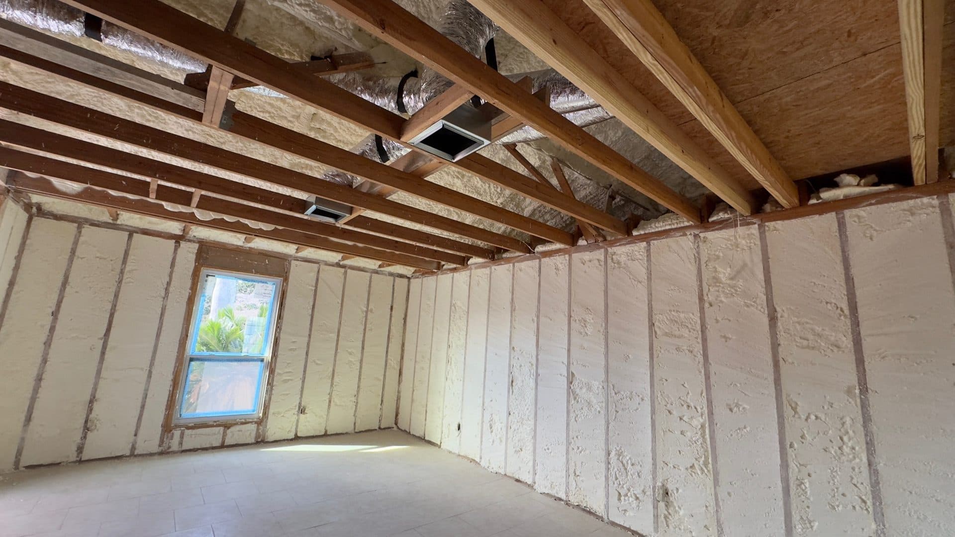 Spray foam insulation fills wall cavities and ceiling joists in a room under construction.