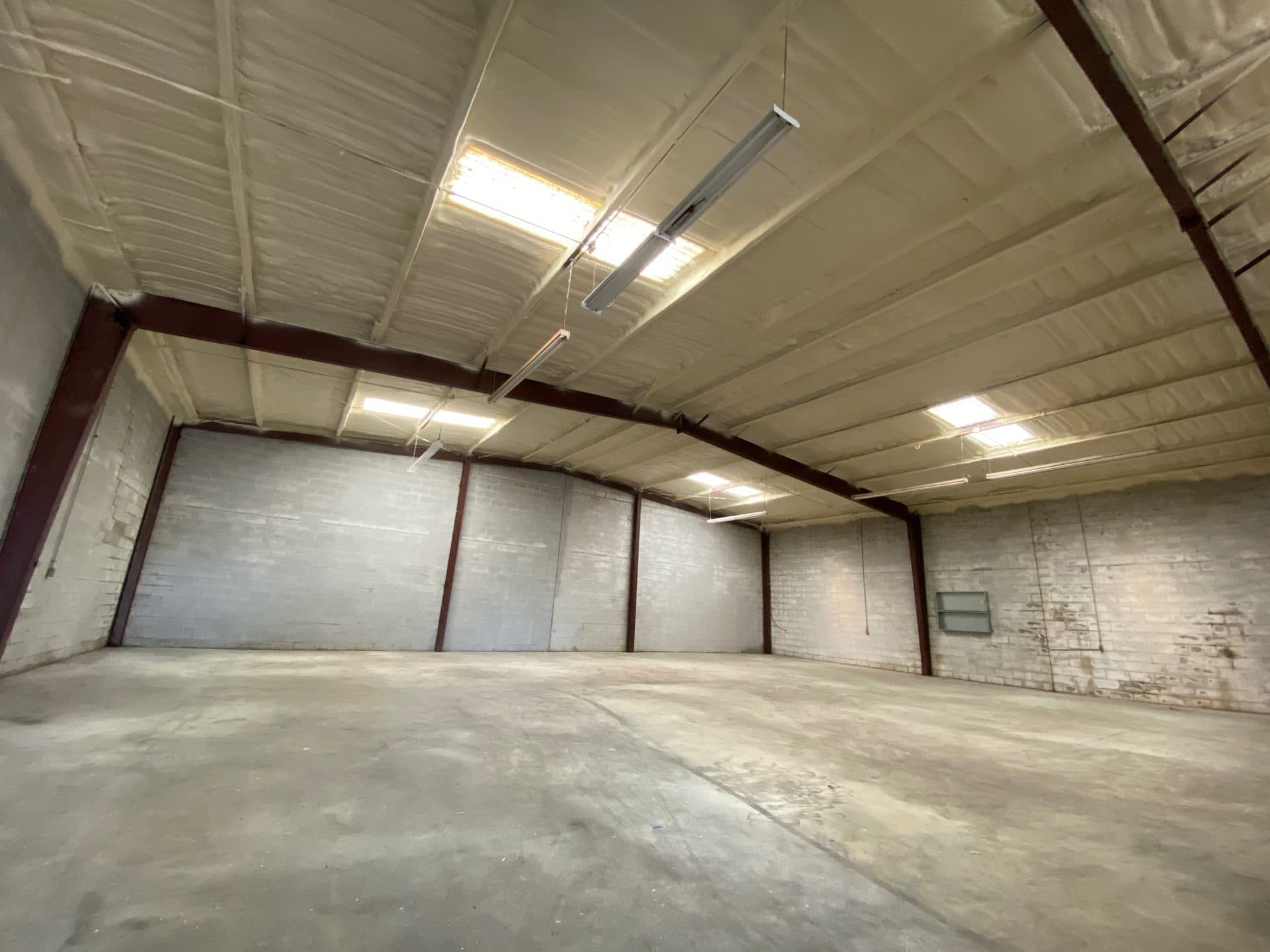 Empty industrial warehouse with concrete floors, cinder block walls, steel beams, and ceiling skylights.