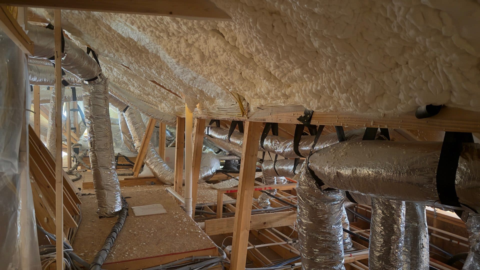 Attic with thick spray foam insulation on the roof and silver flexible HVAC ducts.