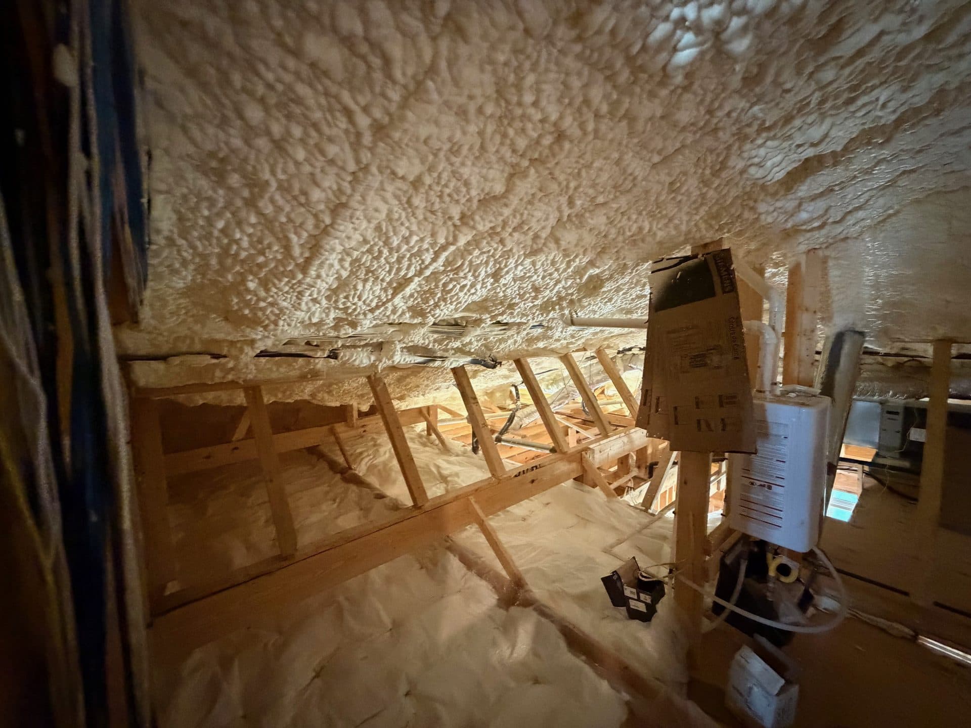 White spray foam insulation applied to the underside of a roof in a wooden attic.