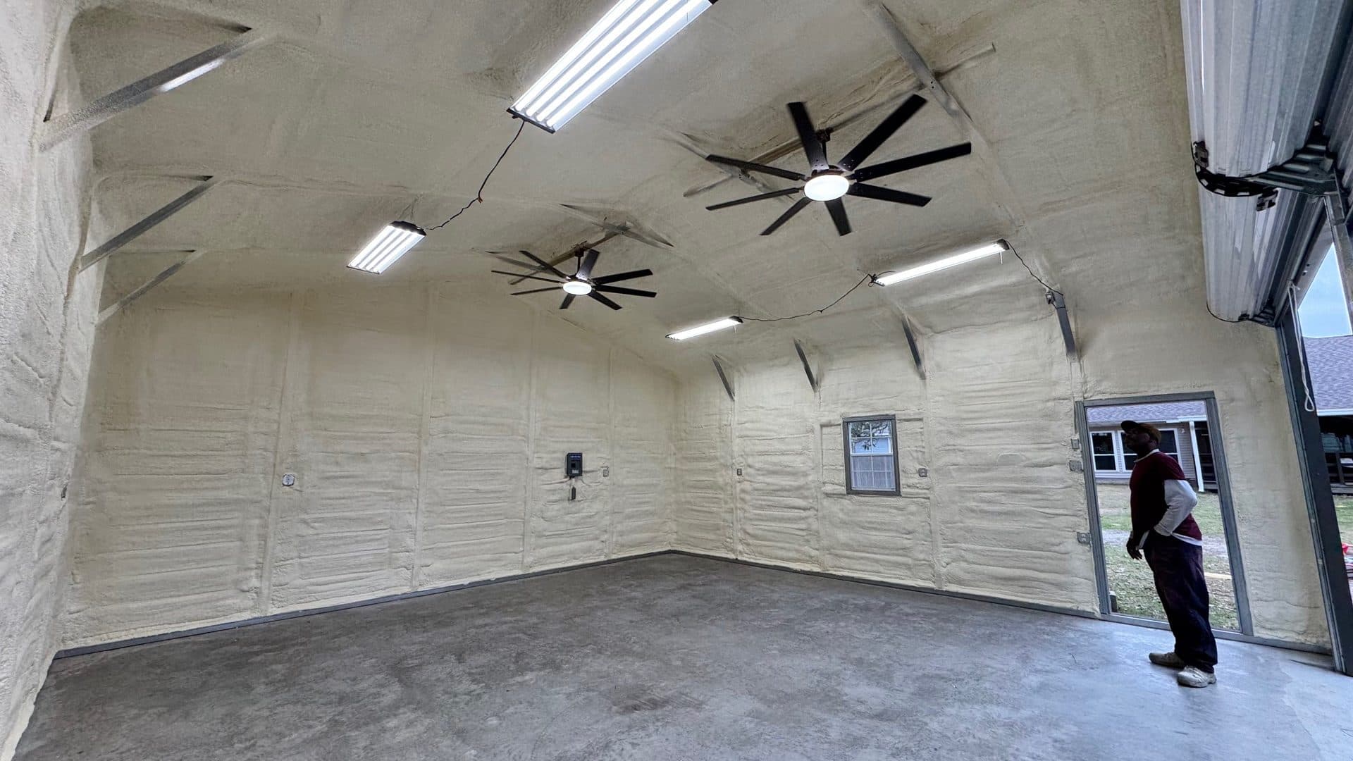 Garage interior featuring spray foam insulation on walls and ceiling with ceiling fans and lights.