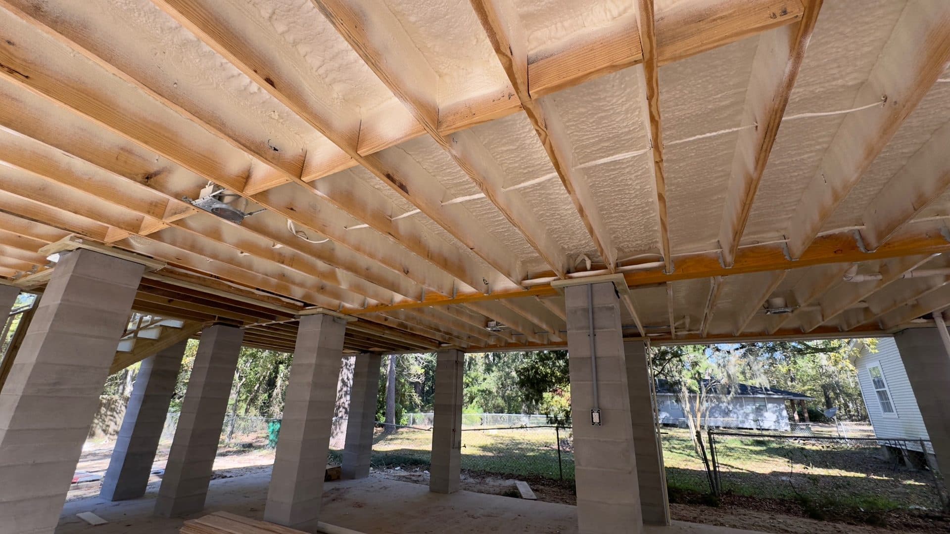 Spray foam insulation applied between wooden joists of an elevated structure on concrete pillars.