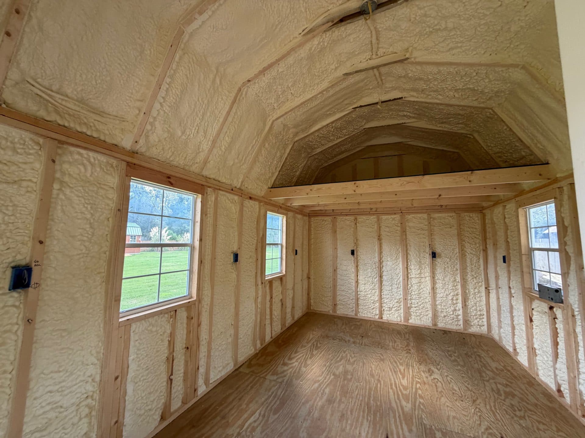 Interior of a wooden shed with spray foam insulation, plywood flooring, and a small loft.