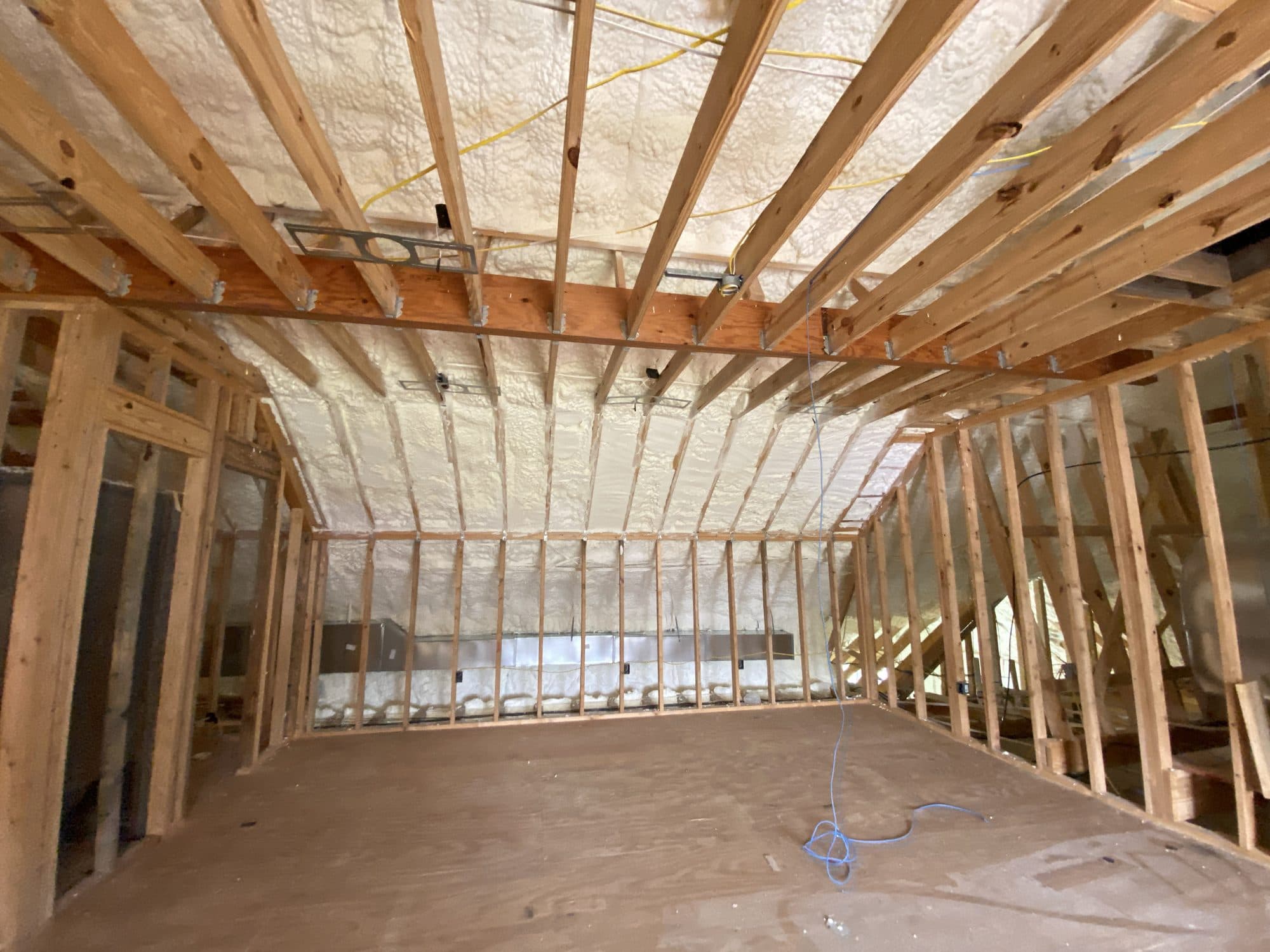 Wooden framing and spray foam insulation in an unfinished room with a vaulted ceiling.