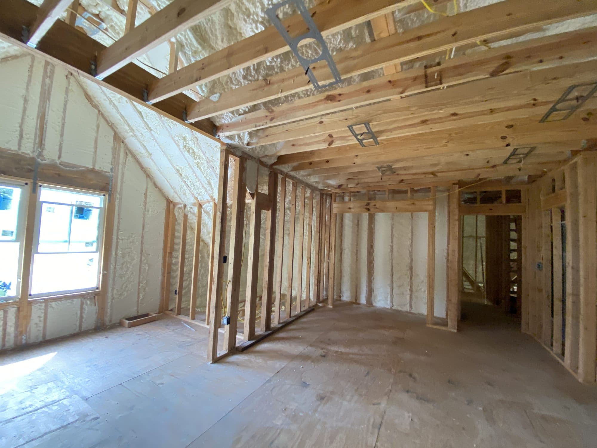 Interior house construction showing wooden framing and spray foam insulation on walls and ceiling.