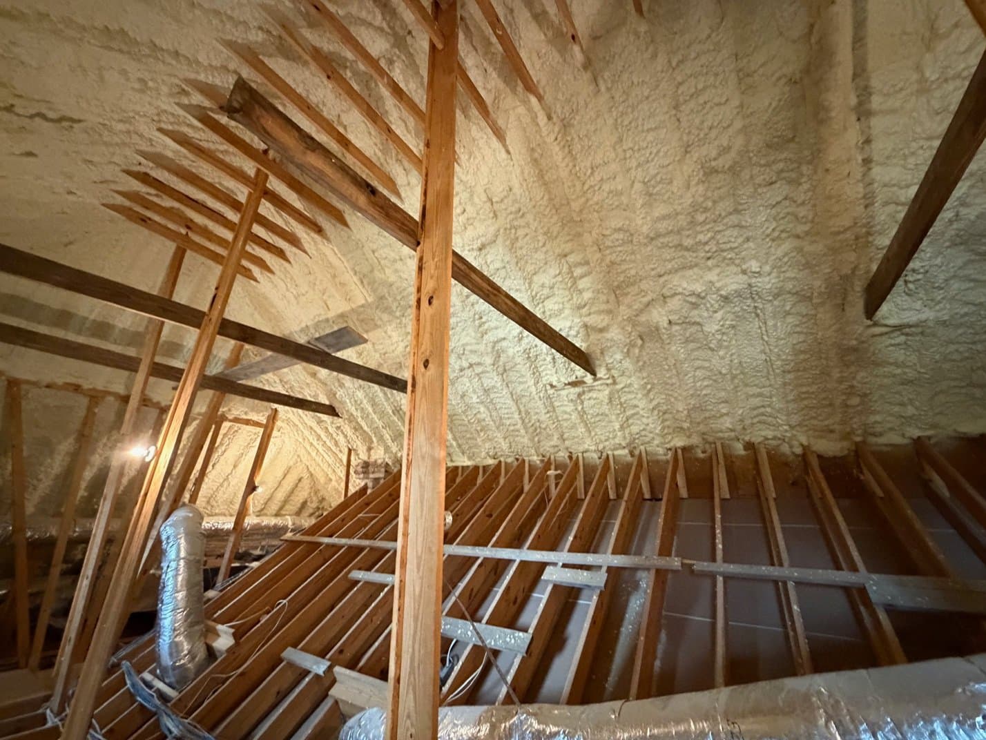 Attic interior featuring wooden rafters and thick spray foam insulation applied to the roof deck.
