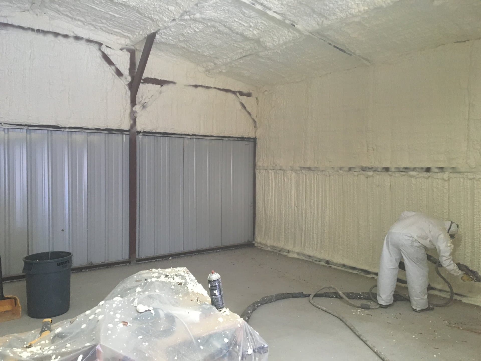 Worker in a white protective suit applying spray foam insulation to a building's interior walls.