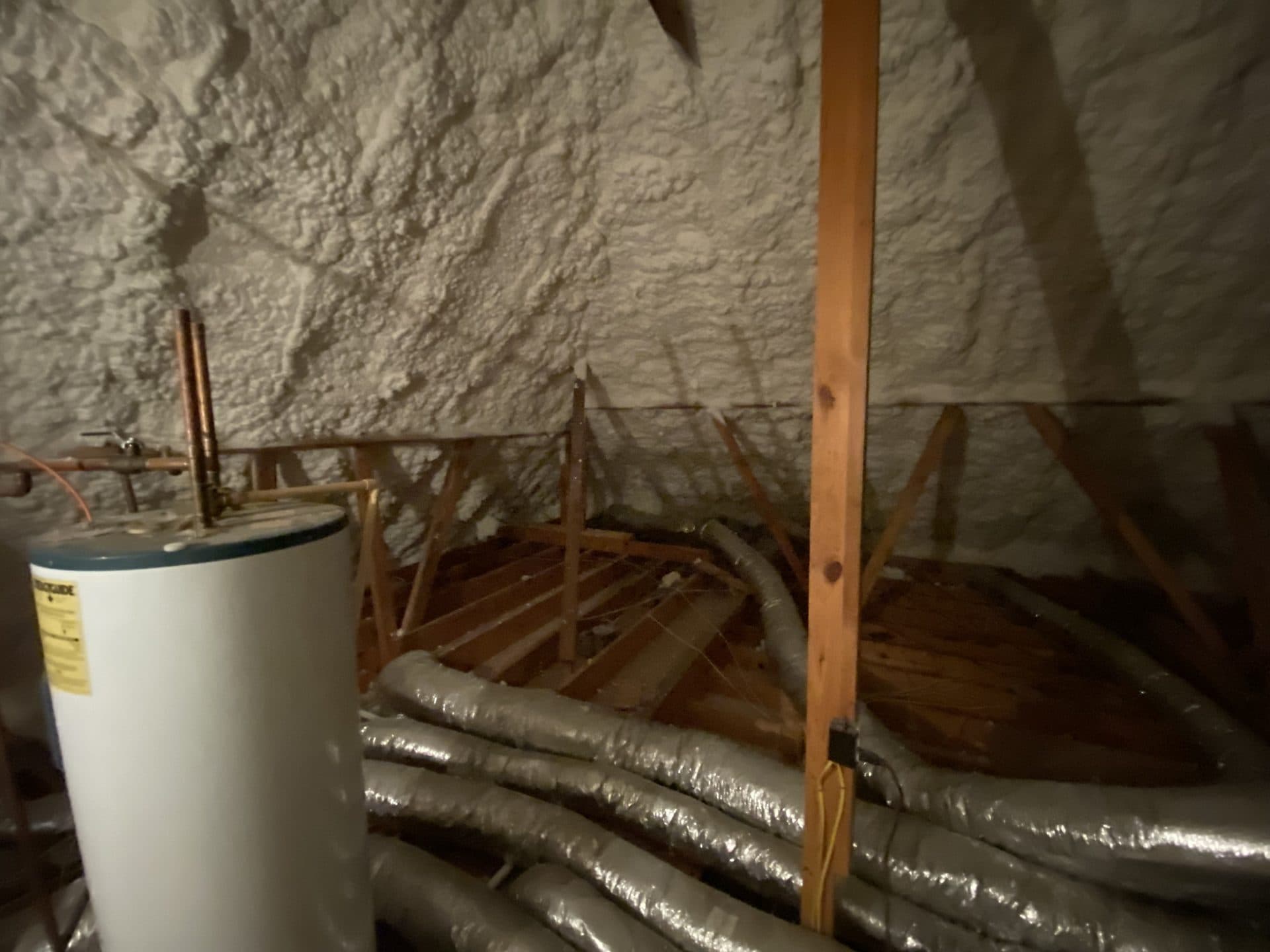 Attic space featuring white spray foam insulation, a water heater, and flexible silver air ducts.