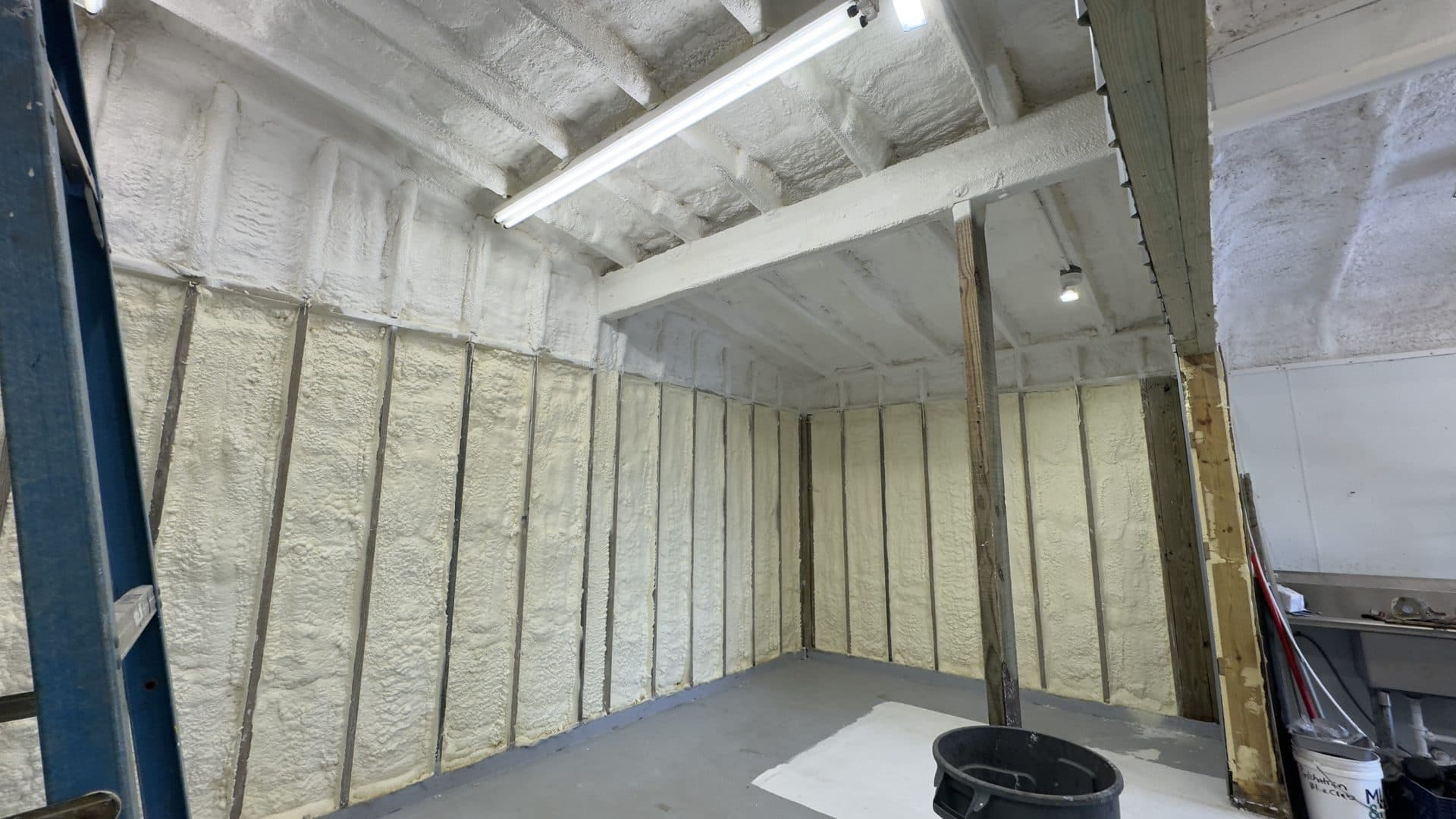 Freshly applied spray foam insulation covers the walls and ceiling of an unfinished room.