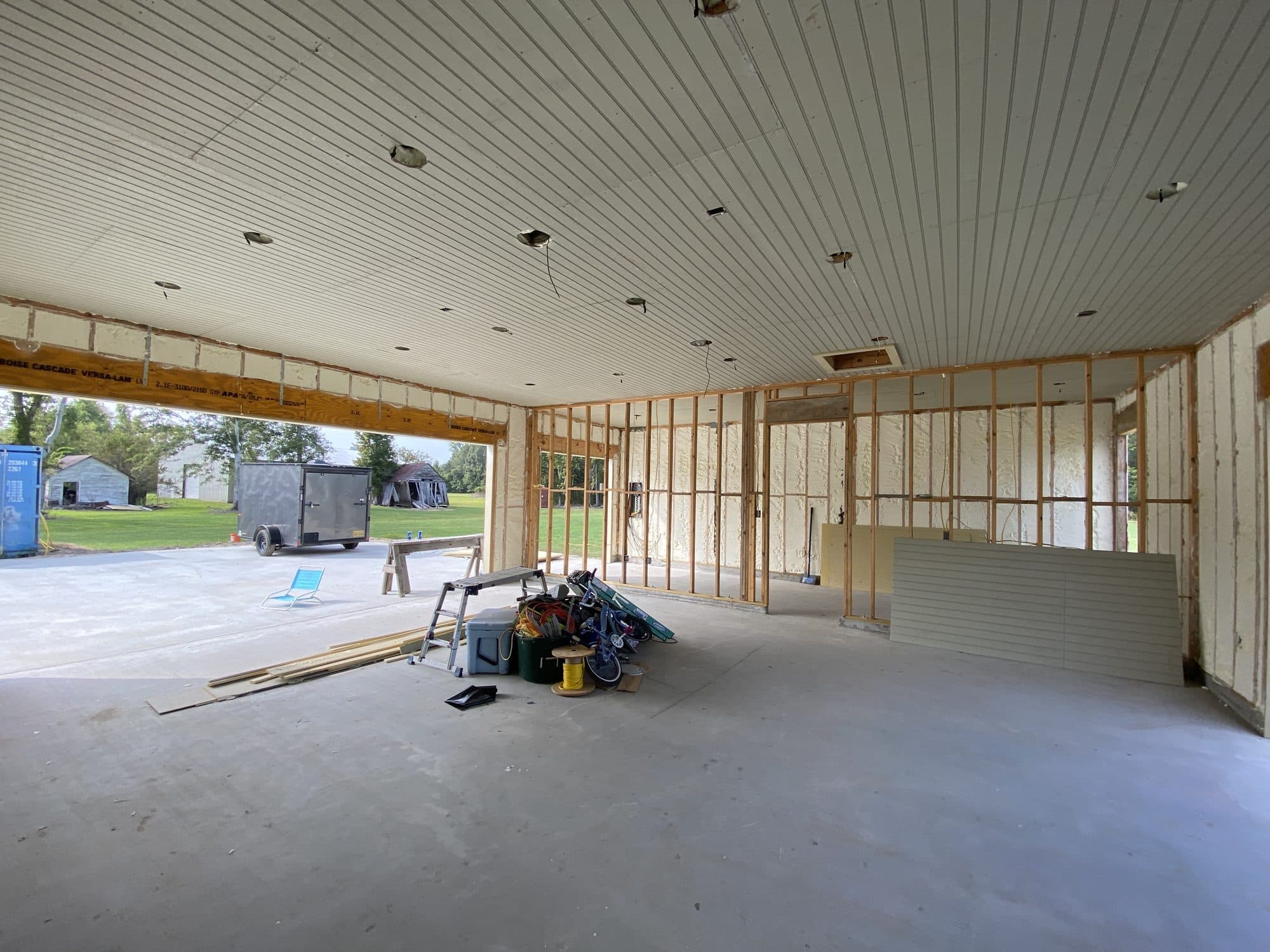 Garage interior under construction with exposed studs, spray foam insulation, and a white paneled ceiling.