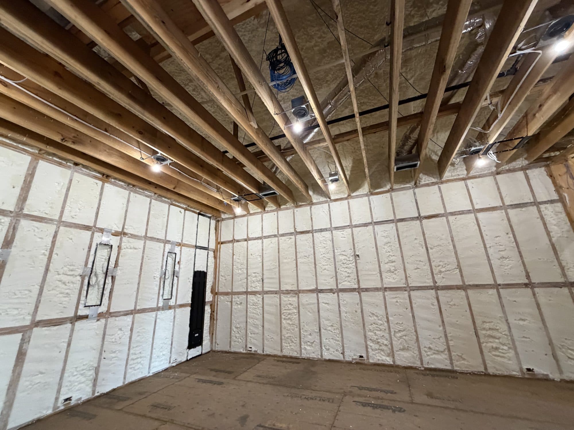 Interior construction site with spray foam insulation on walls and exposed wooden ceiling joists.