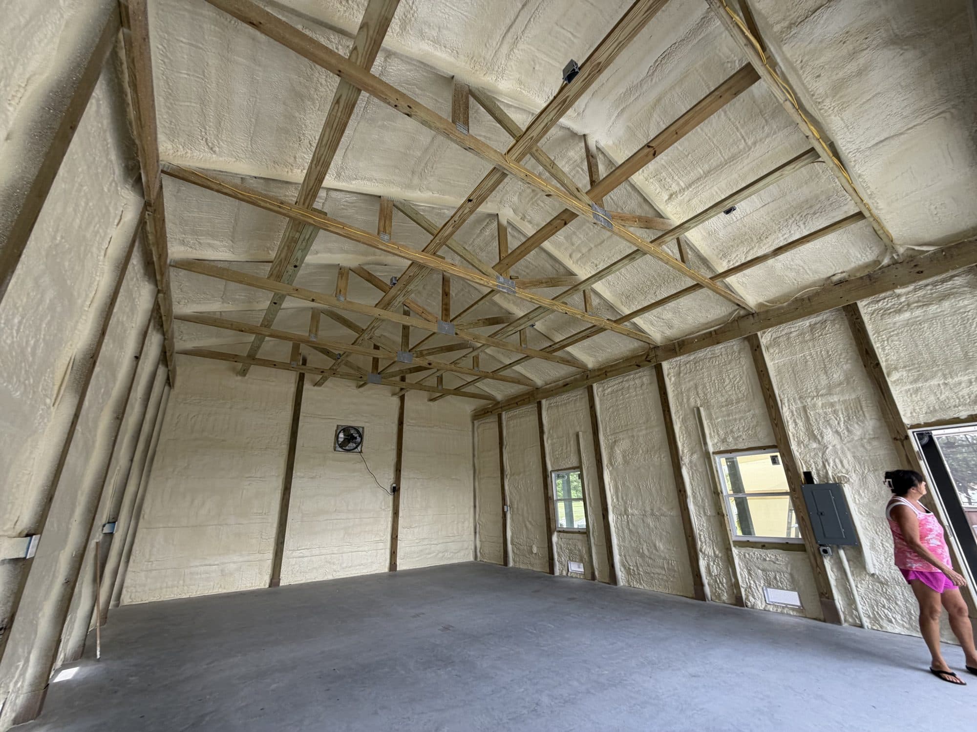 Spray foam insulation covers the interior walls and ceiling of a building with wooden framing.